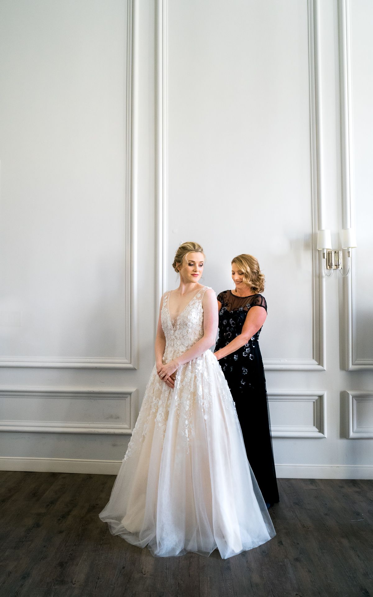 Wedding dress fitting moment in bright white room with classic architectural details.