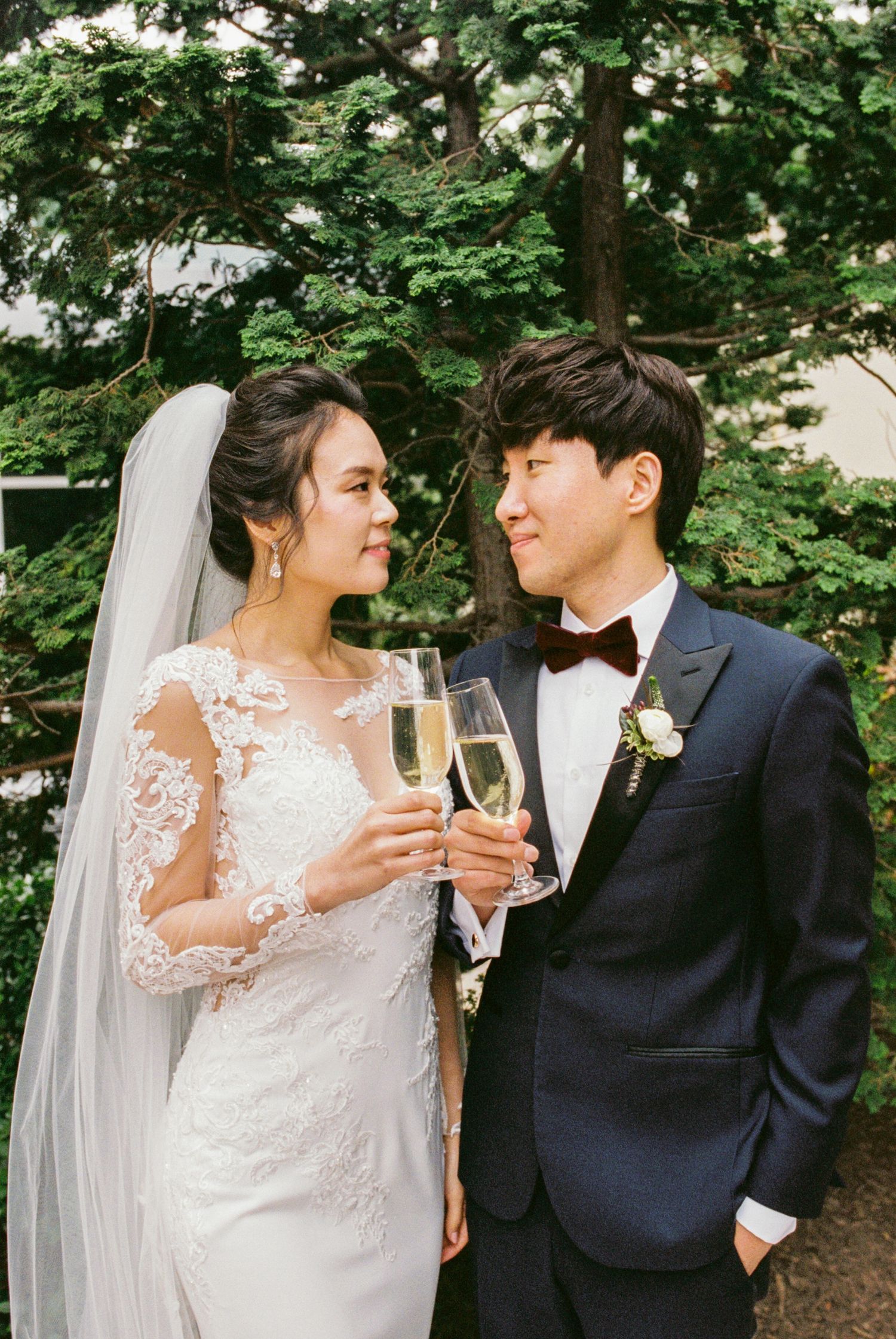 Joyful newlyweds toasting champagne in garden setting with bride in elegant lace gown.