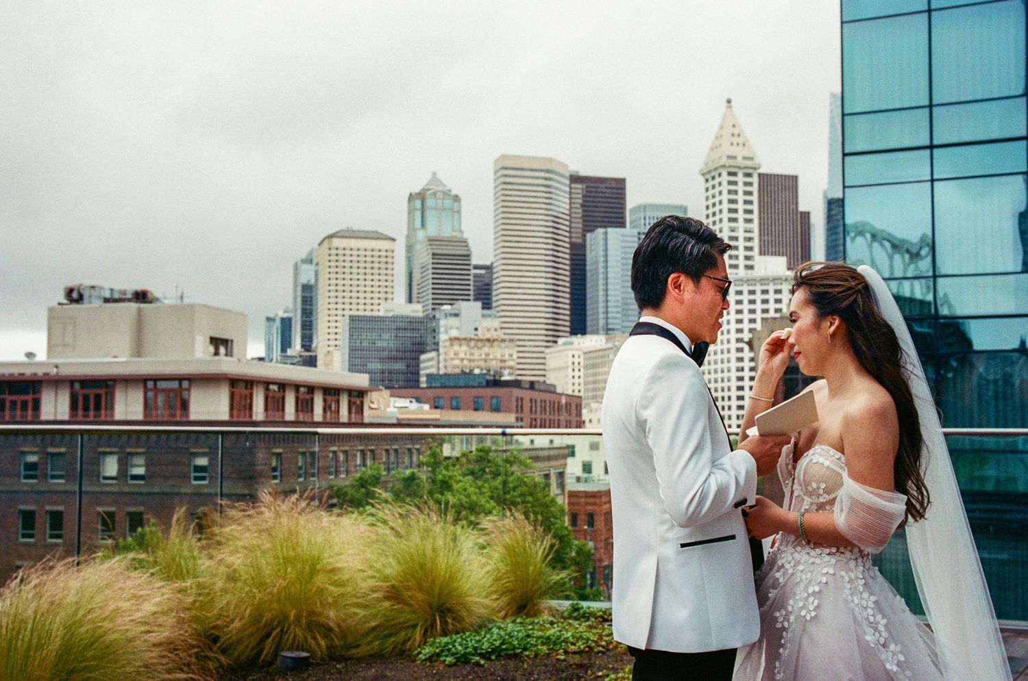 Couple shares romantic moment against urban skyline backdrop with modern glass buildings.