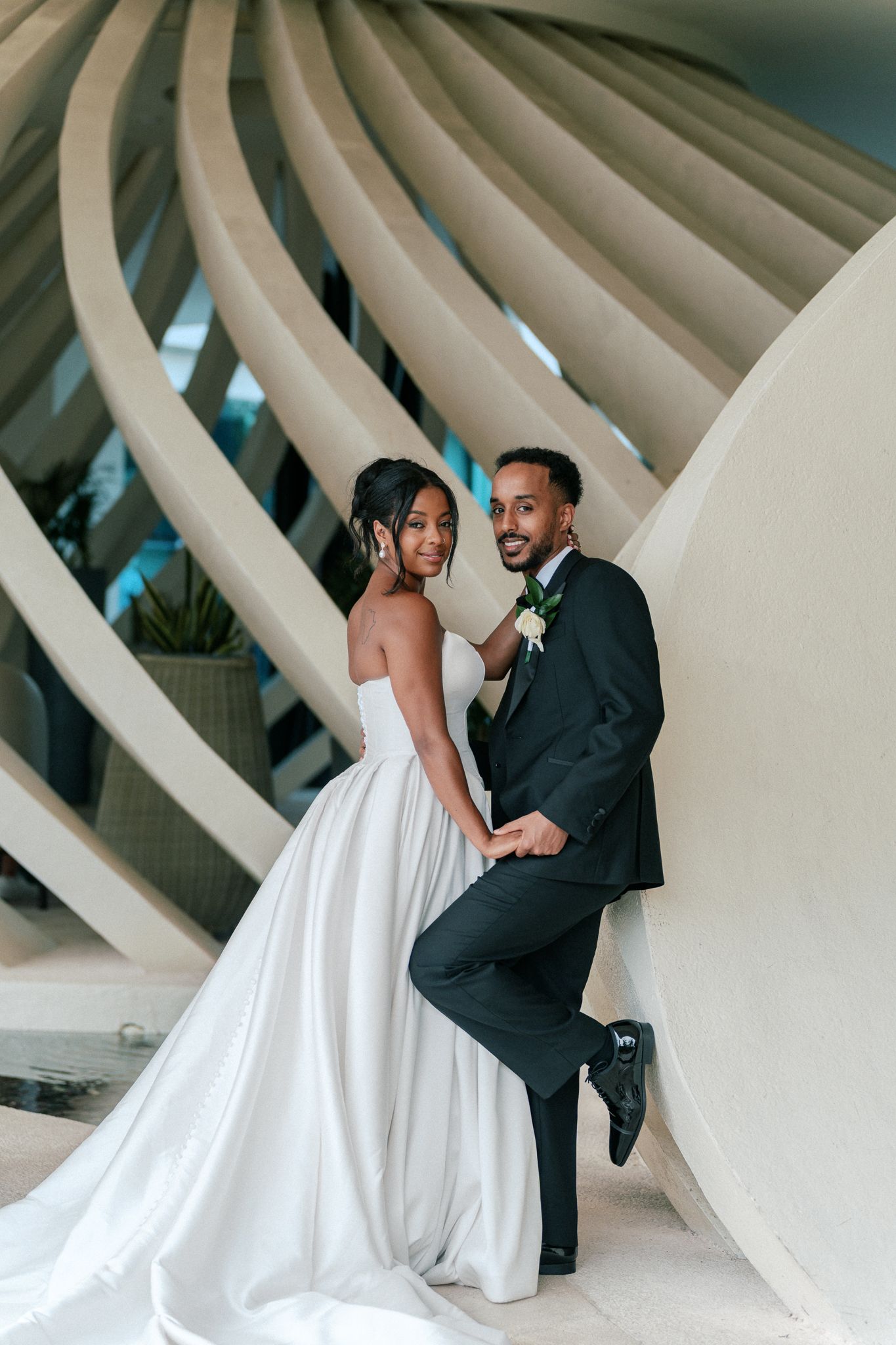 Elegant bride and groom posing together in front of sweeping architectural curves on their wedding day.