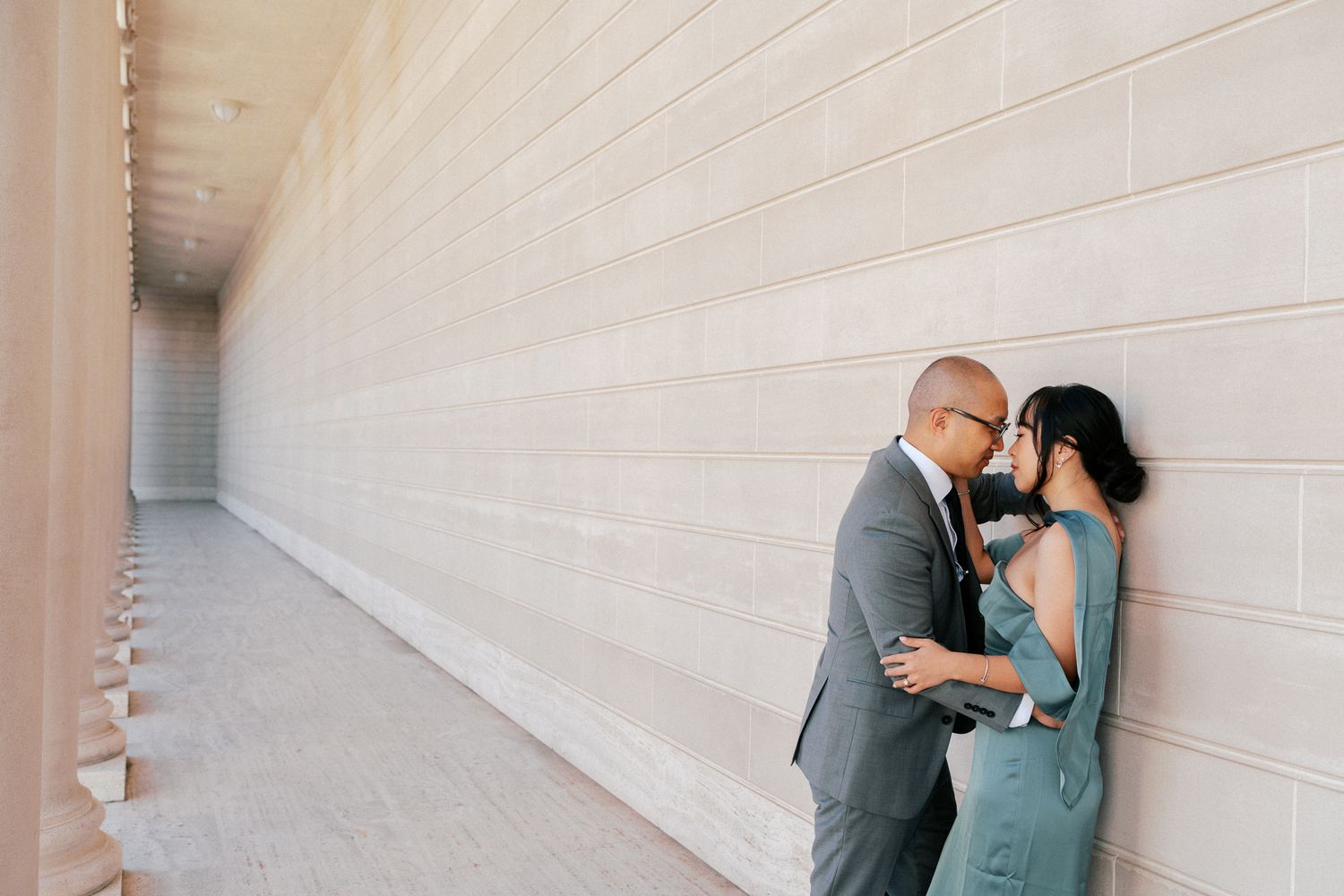 Couple sharing a romantic moment leaning against a modern stone wall in an outdoor corridor.