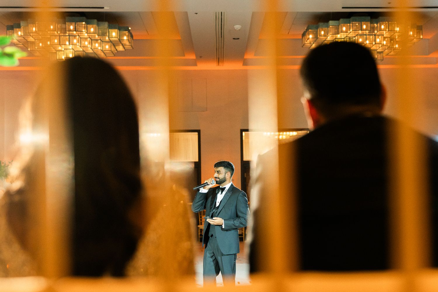 Wedding celebration in a grand ballroom with dramatic orange lighting and silhouettes.