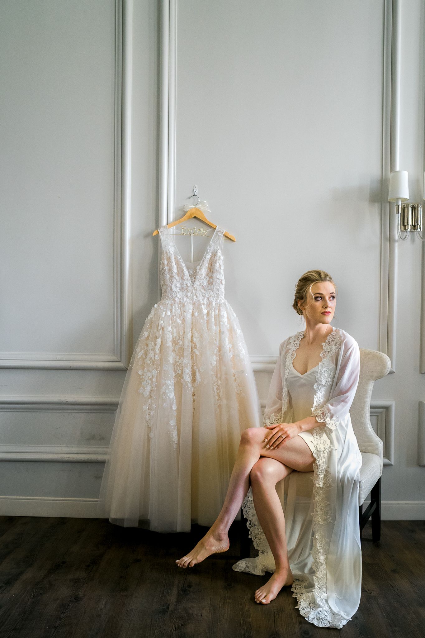 Bridal boudoir session with wedding dress display in minimalist white room.