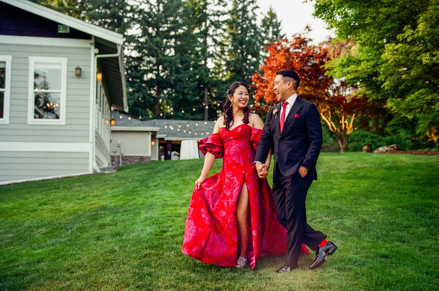 Couple walking on lawn in formal red dress and navy suit by white house.