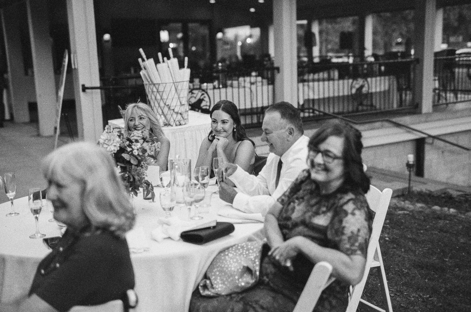 Black and white photo of guests laughing and enjoying themselves at a wedding reception dinner table.