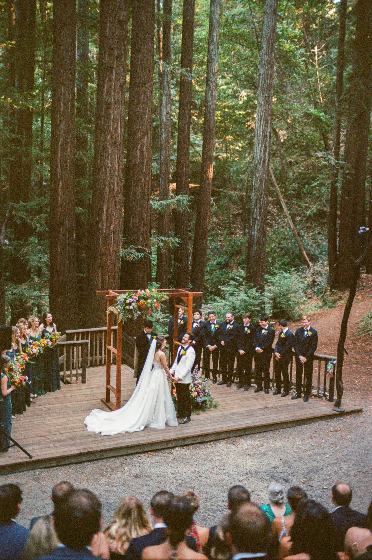 Outdoor wedding ceremony setup in a redwood forest with wooden benches and floral decorations.