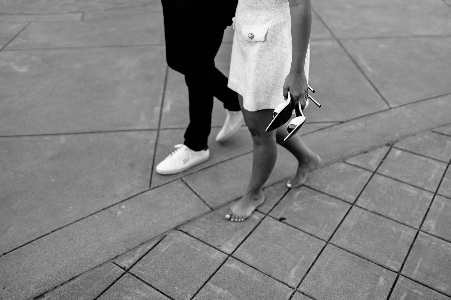 Black and white sequence of feet walking on patterned pavement with a shopping bag visible in the frame.