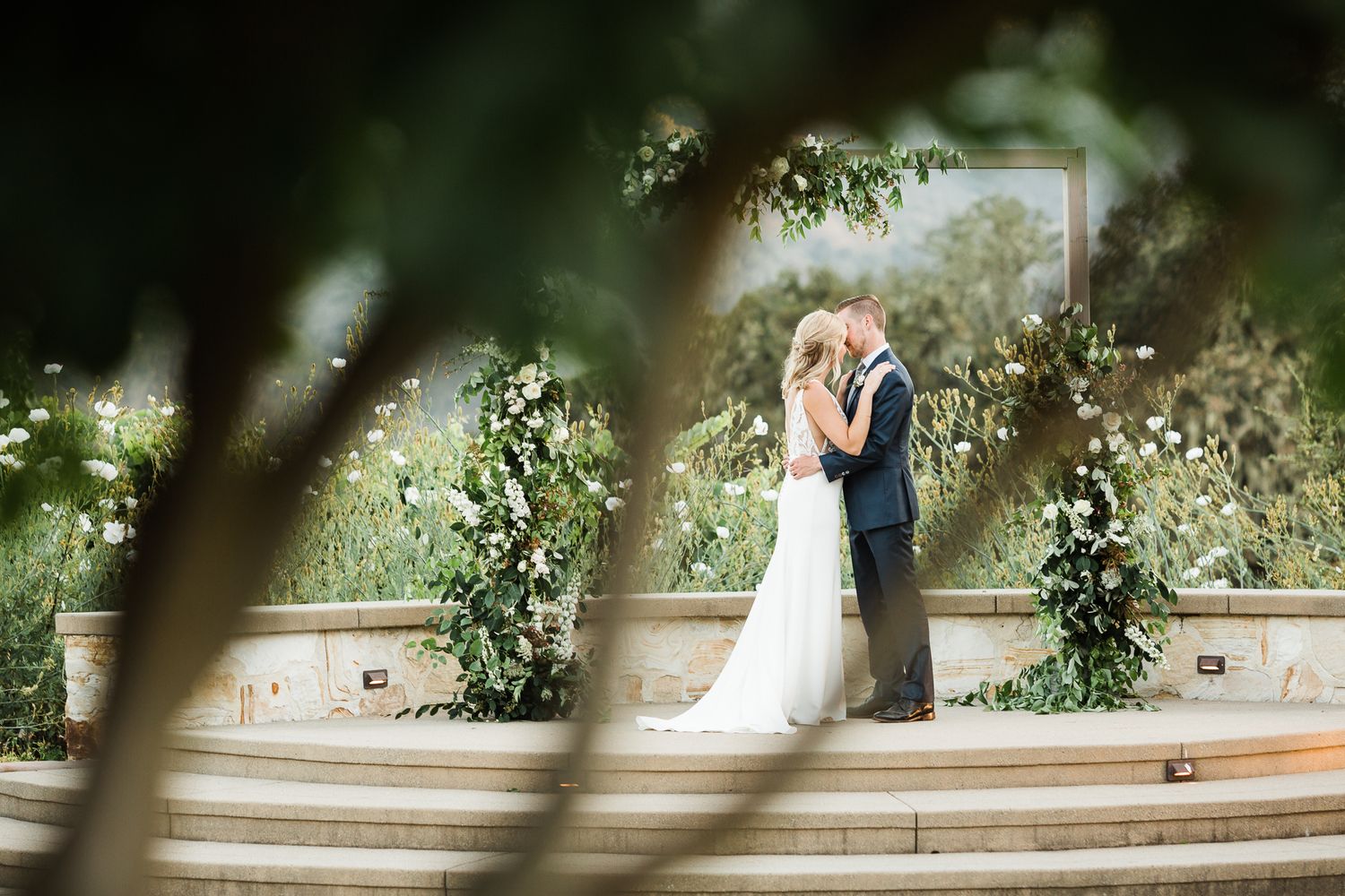 Artistic wedding photography through foliage showing romantic moments in a garden setting.