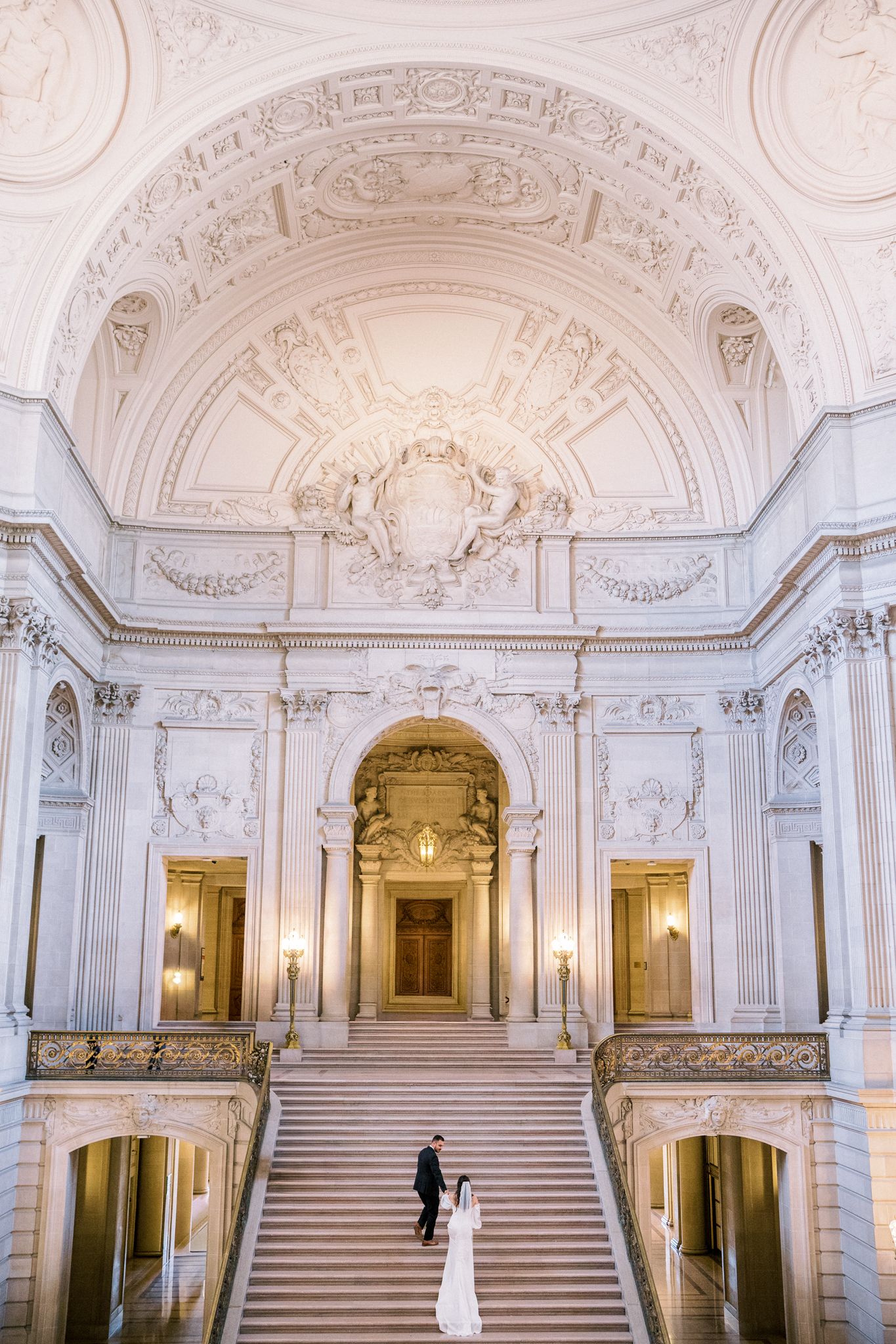 Ornate white marble staircase in grand historic building with elaborate architectural details and golden accents.