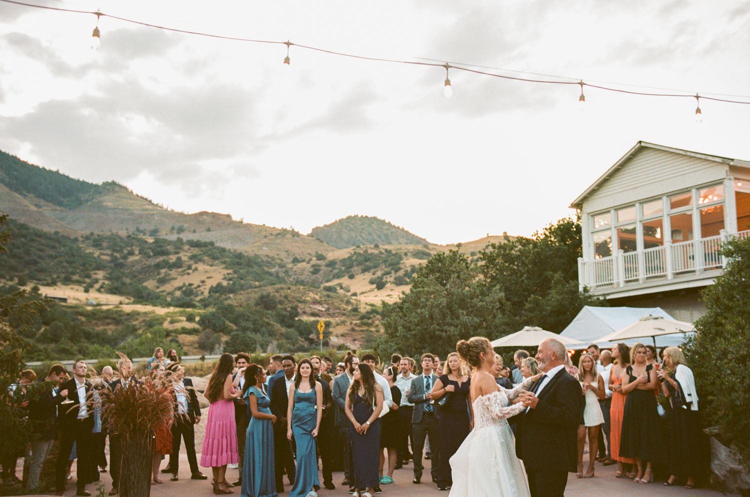 Outdoor wedding reception under string lights with mountain landscape backdrop.