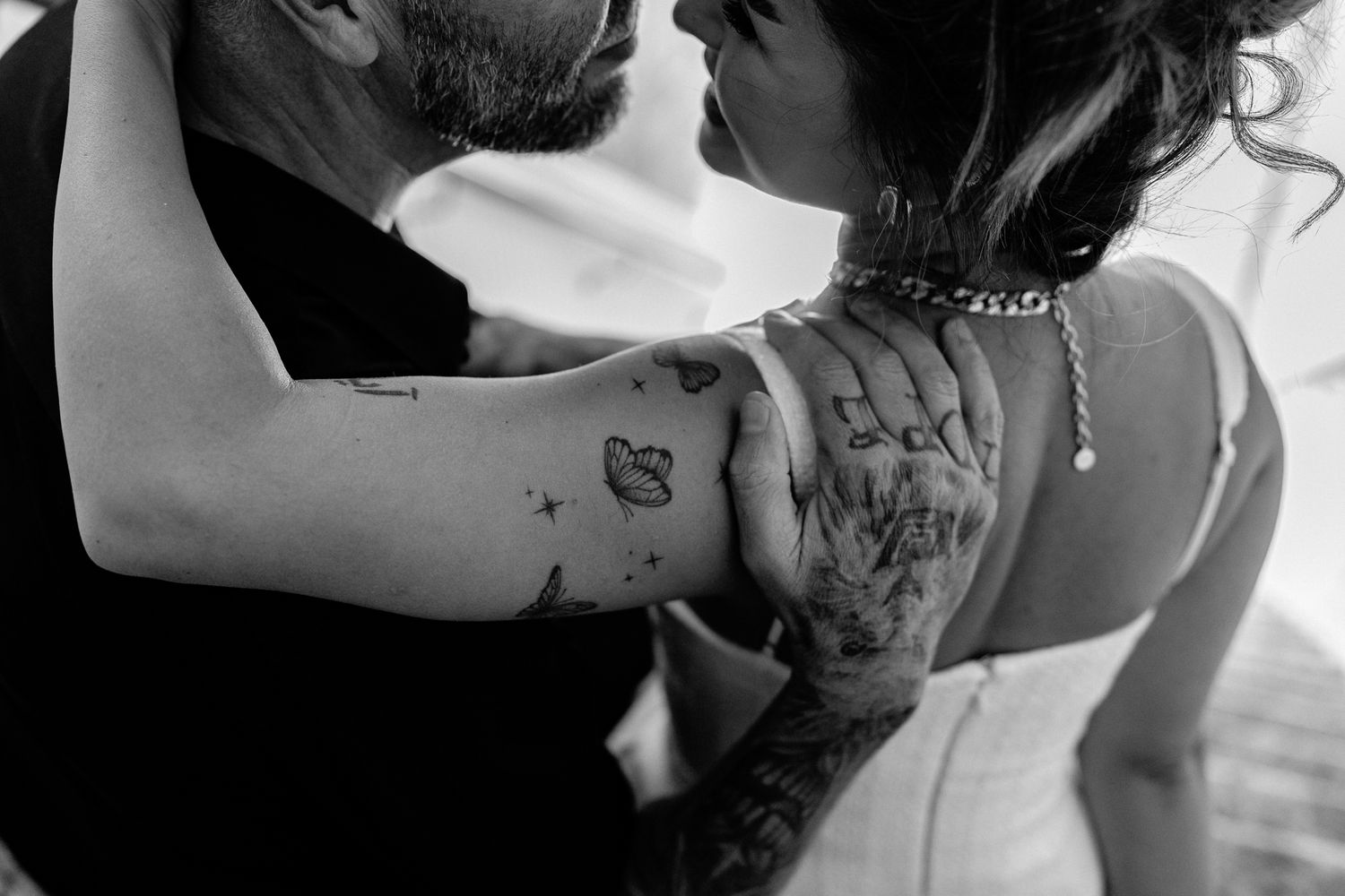 Black and white close-up photo of a couple embracing, showing detailed back tattoos on one person.