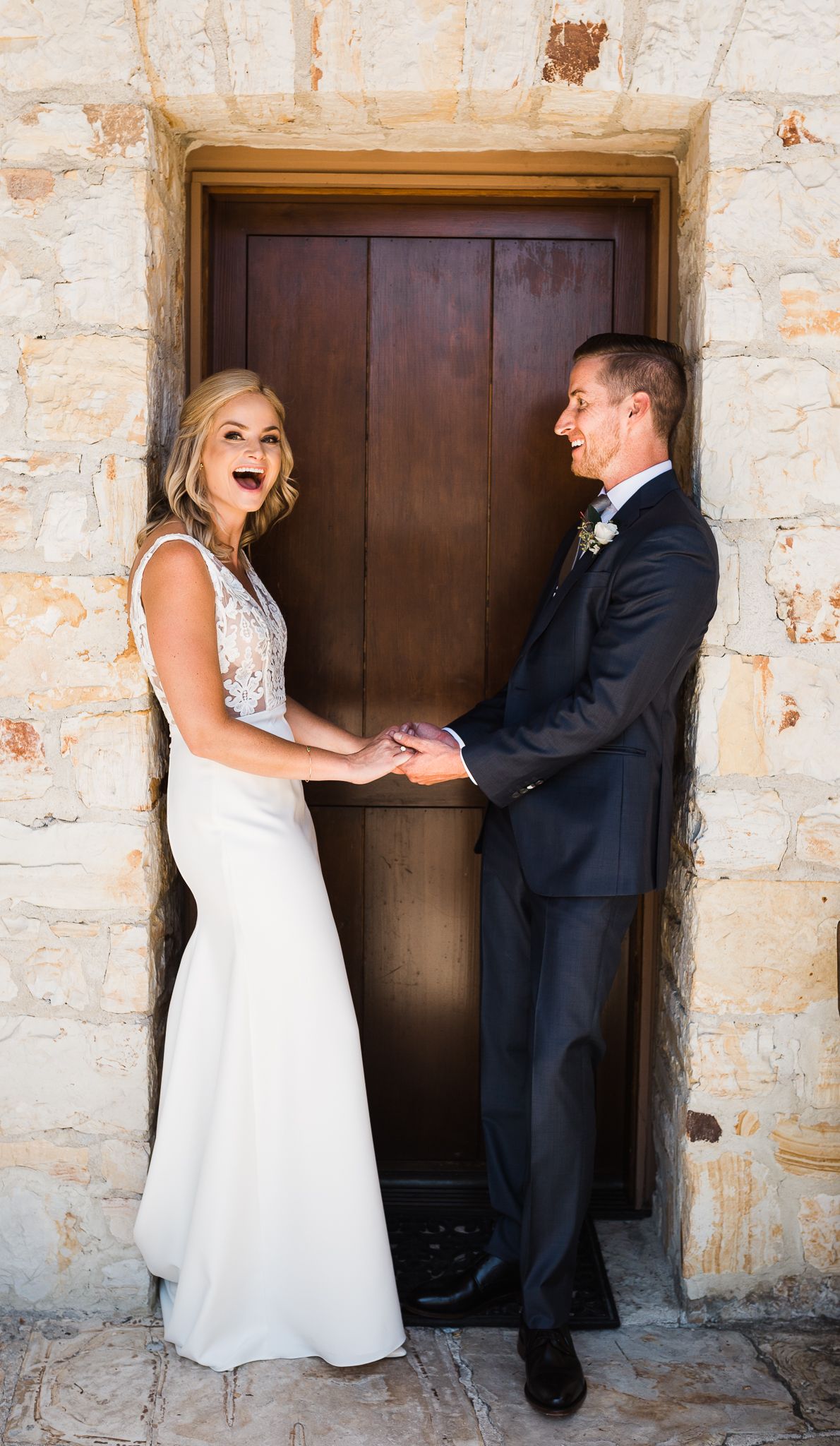 Playful first look sequence between couple against rustic stone wall and wooden doors.