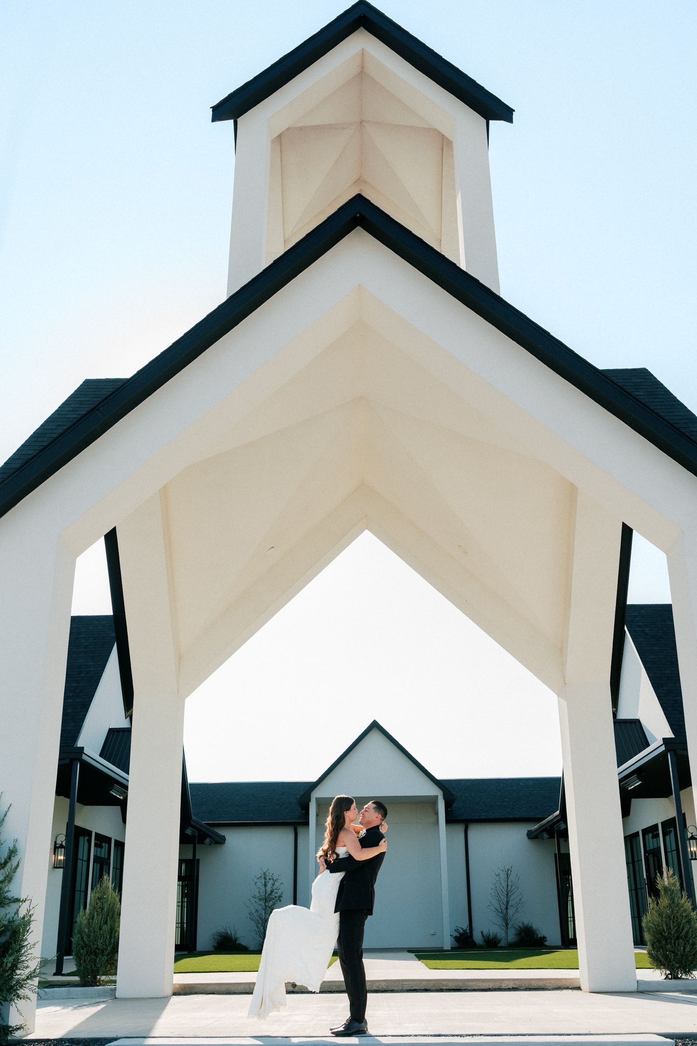 Couple embracing under white church arch with black trim at elegant wedding venue.