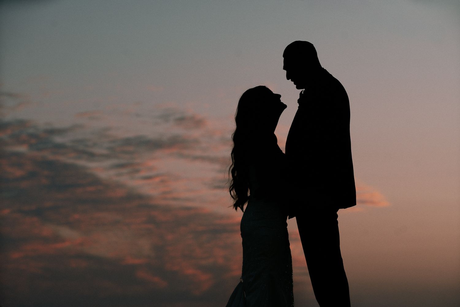 Romantic silhouette of a couple facing each other against a colorful sunset sky with pink and blue hues.