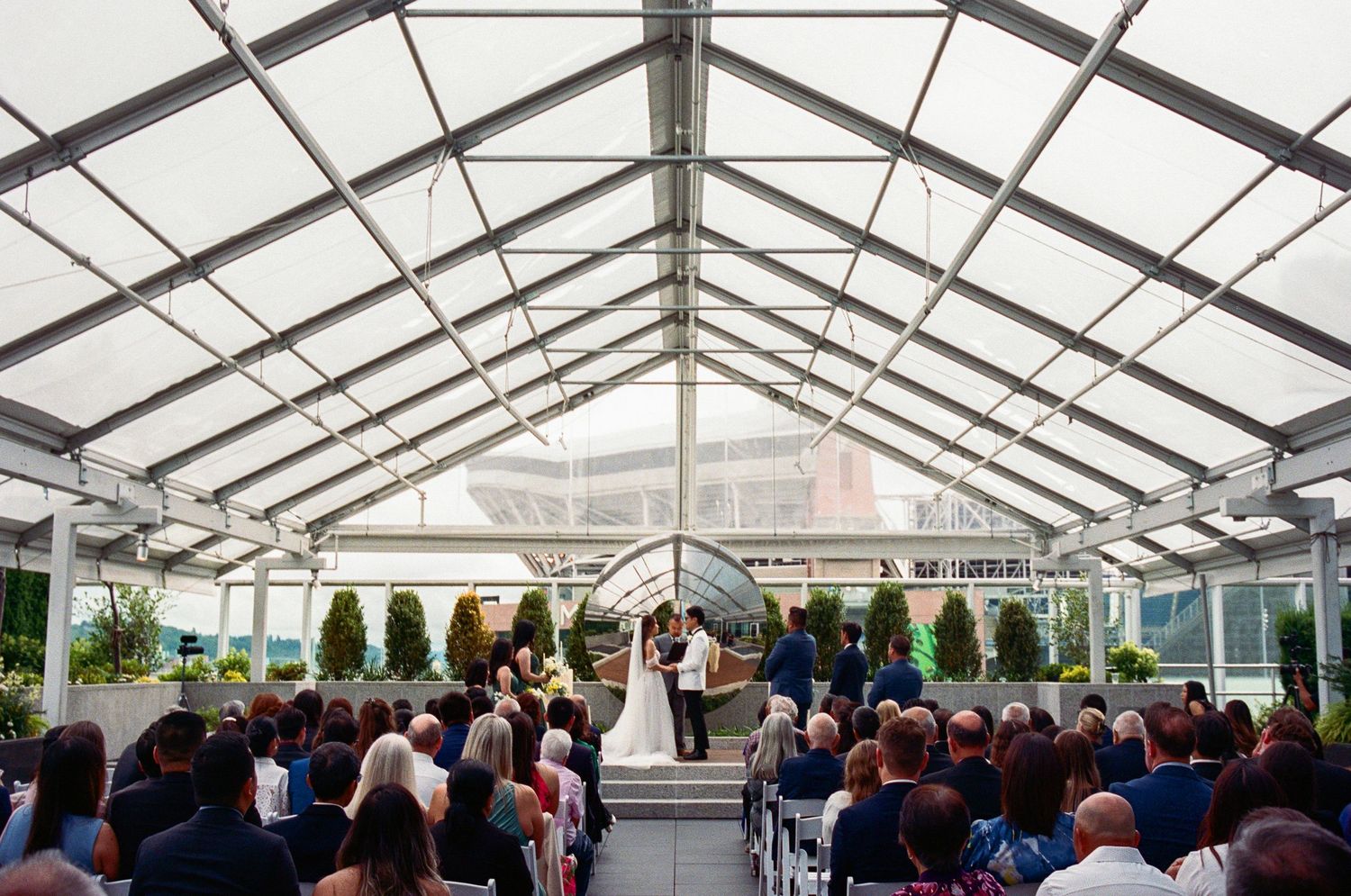 Large white tent wedding ceremony venue filled with guests seated in rows.