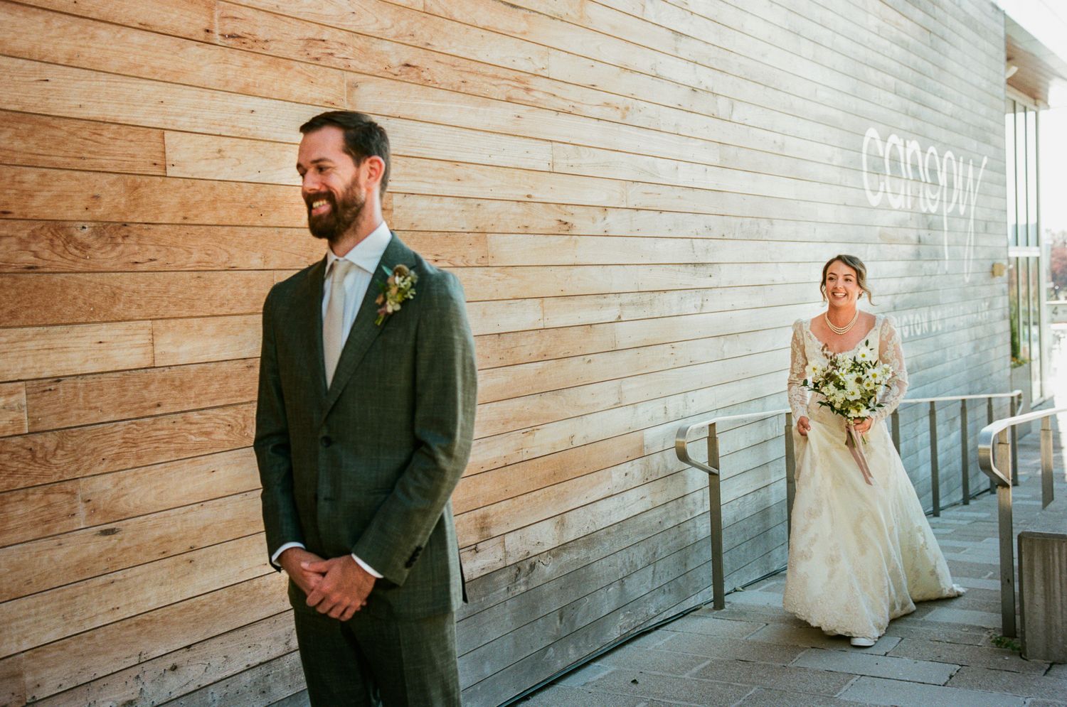 First look wedding moment with couple positioned against wooden wall during outdoor ceremony.