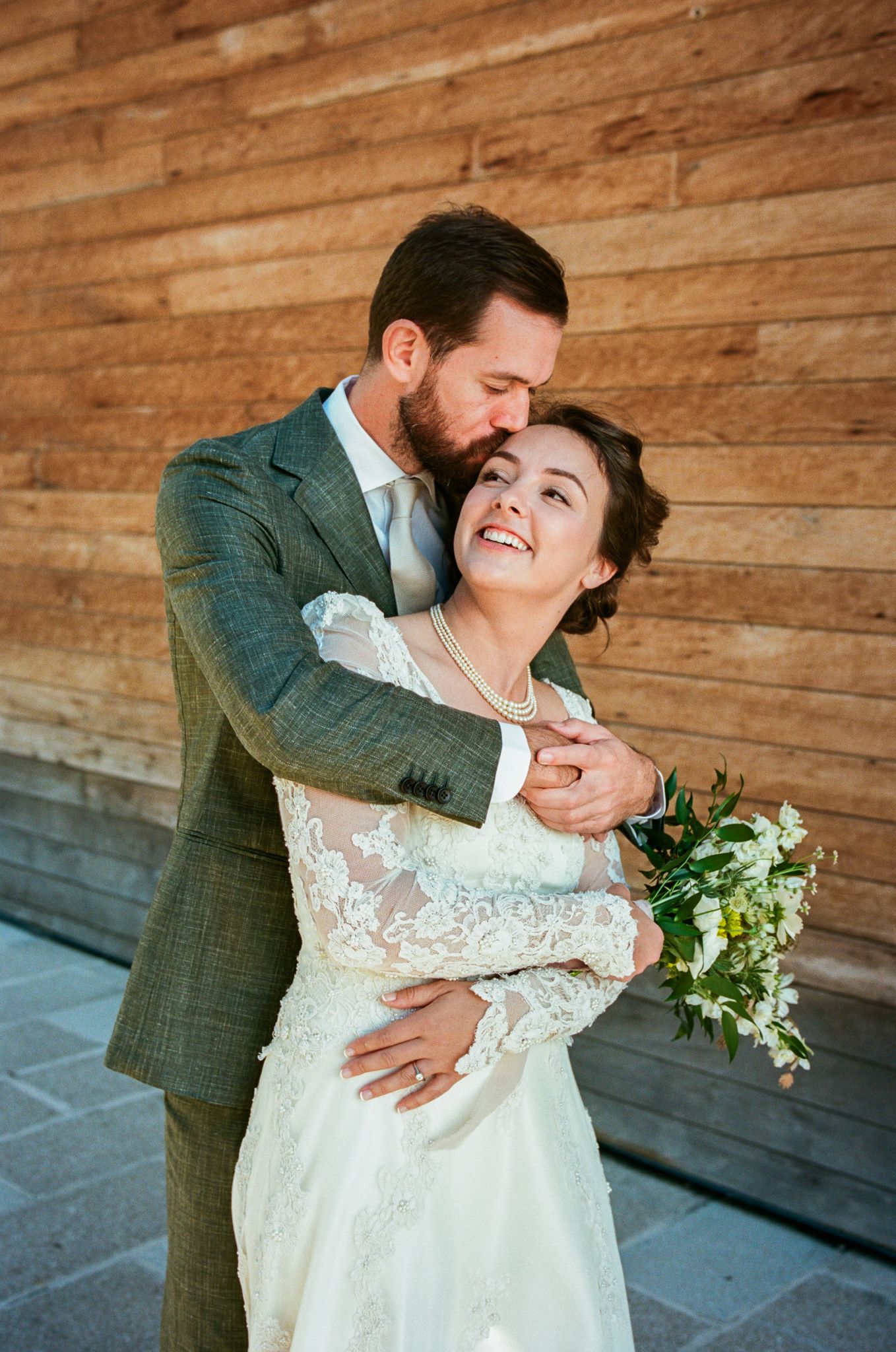 Romantic wedding portrait of a couple embracing against a rustic wooden wall background.