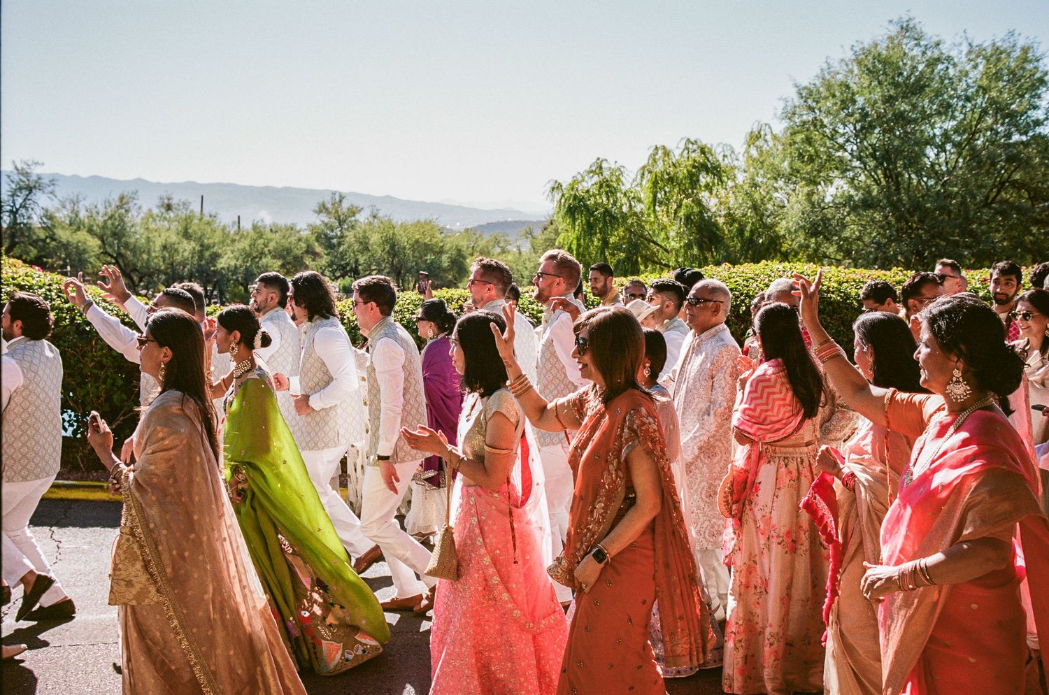 Wedding party members in coral and white attire celebrate during an outdoor ceremony.