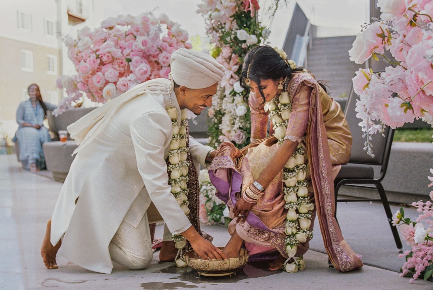 Sikh wedding couple performing ritual with flower garlands at floral altar.