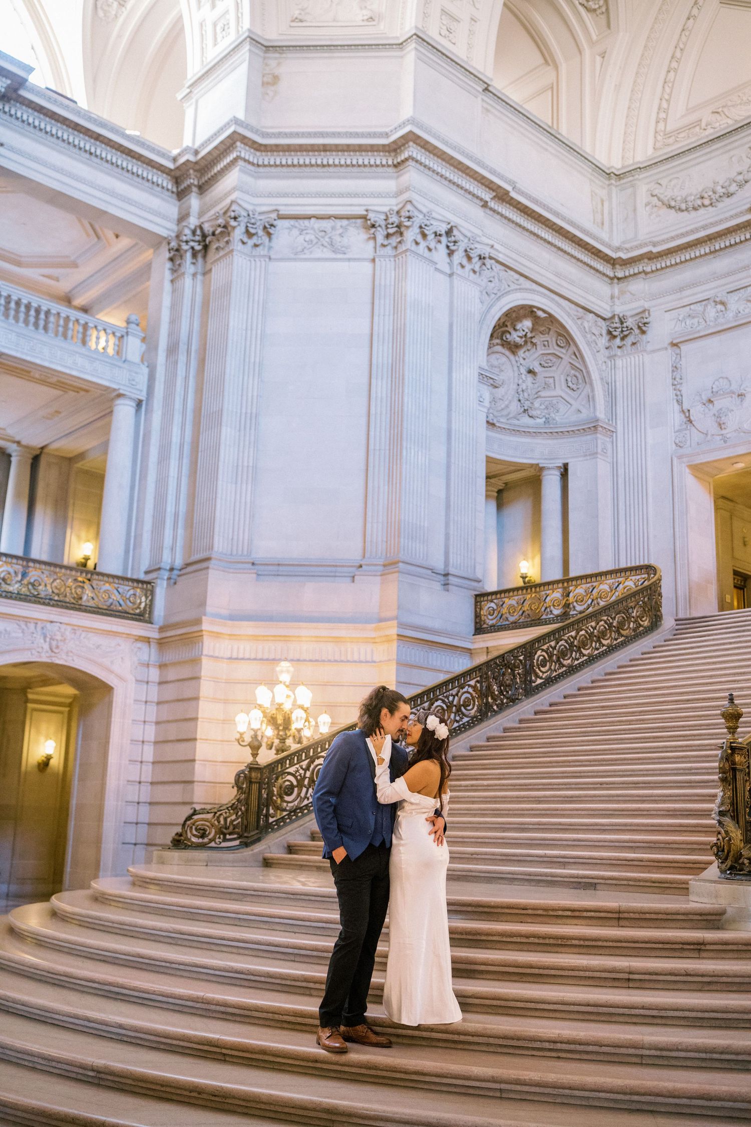 A couple shares an intimate moment on the grand marble staircase inside San Francisco City Hall's ornate interior.