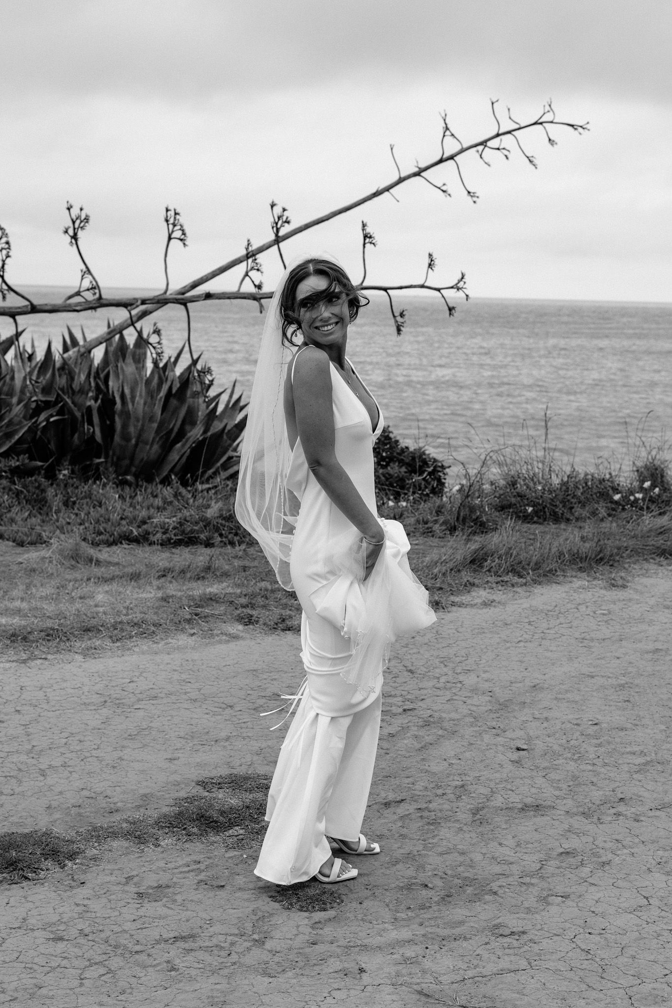 Elegant bridal portrait against coastal landscape in black and white.