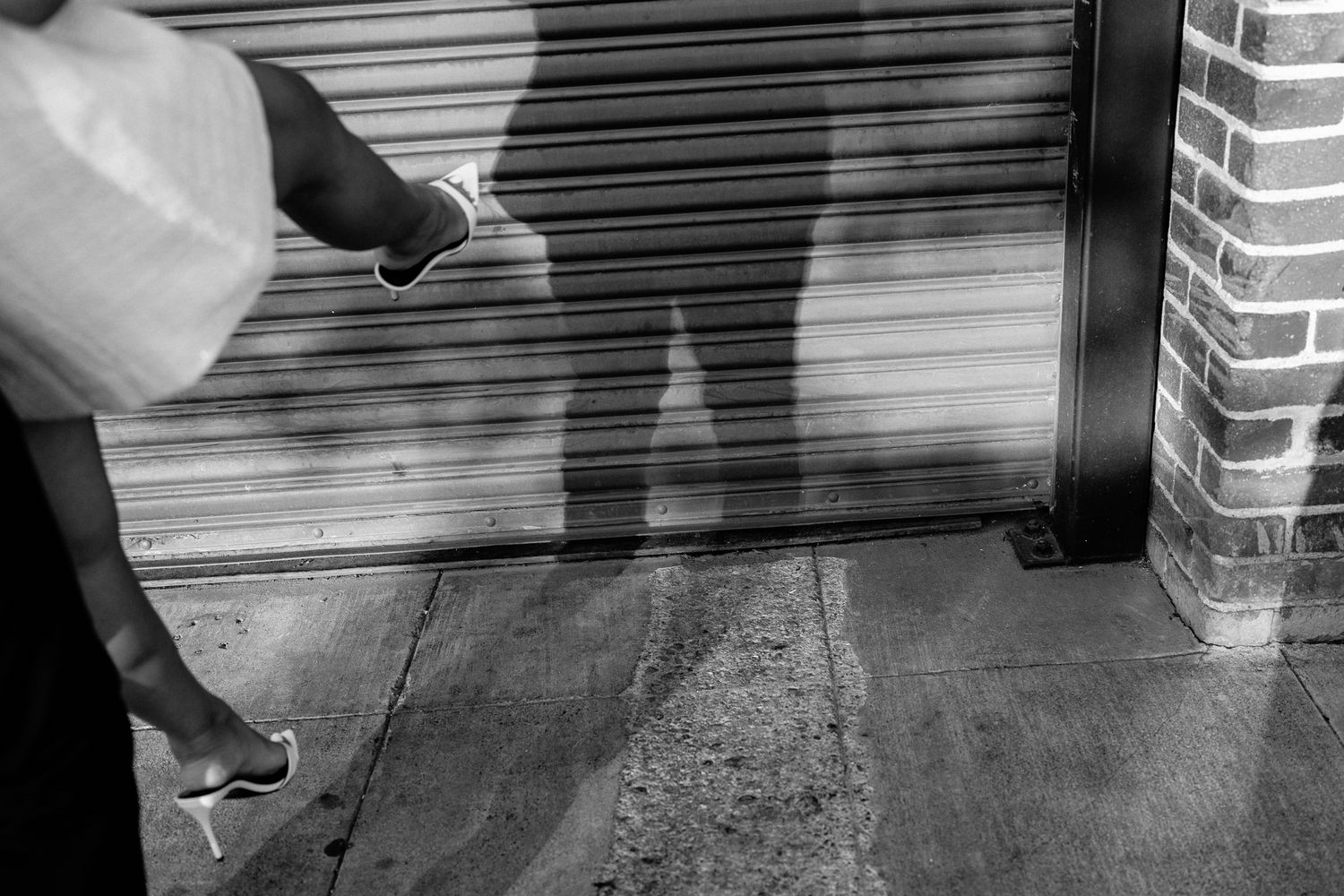 Black and white security camera footage shows a person crouching to inspect or adjust something near a doorway.