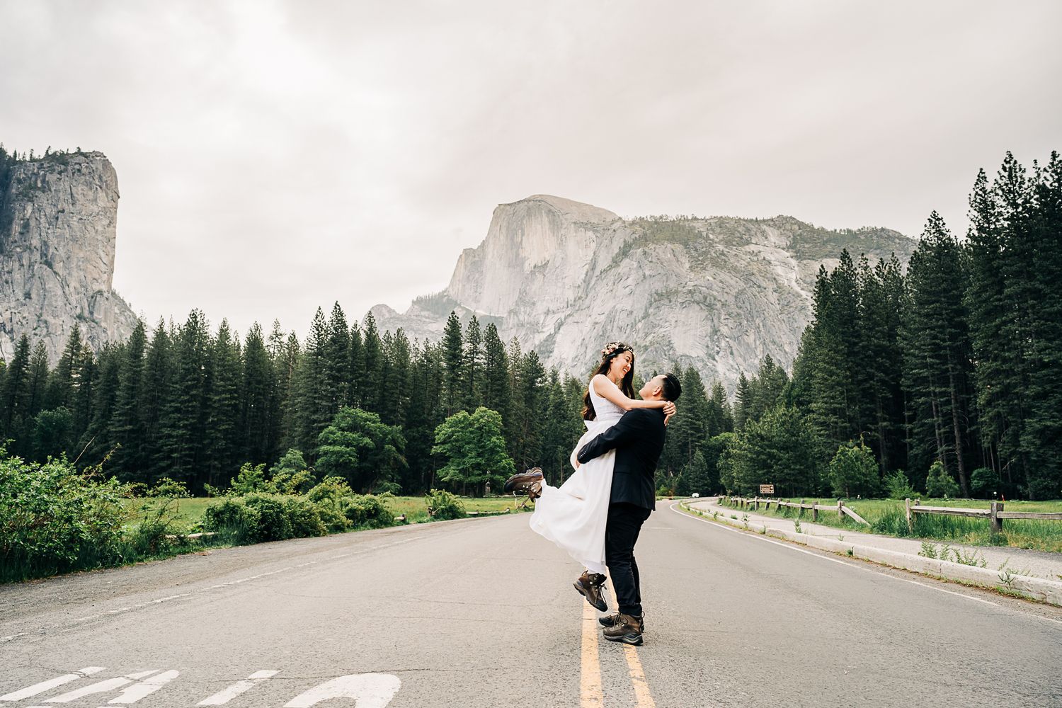 A romantic couple dances together in front of majestic mountain peaks and evergreen forests in a scenic outdoor setting.