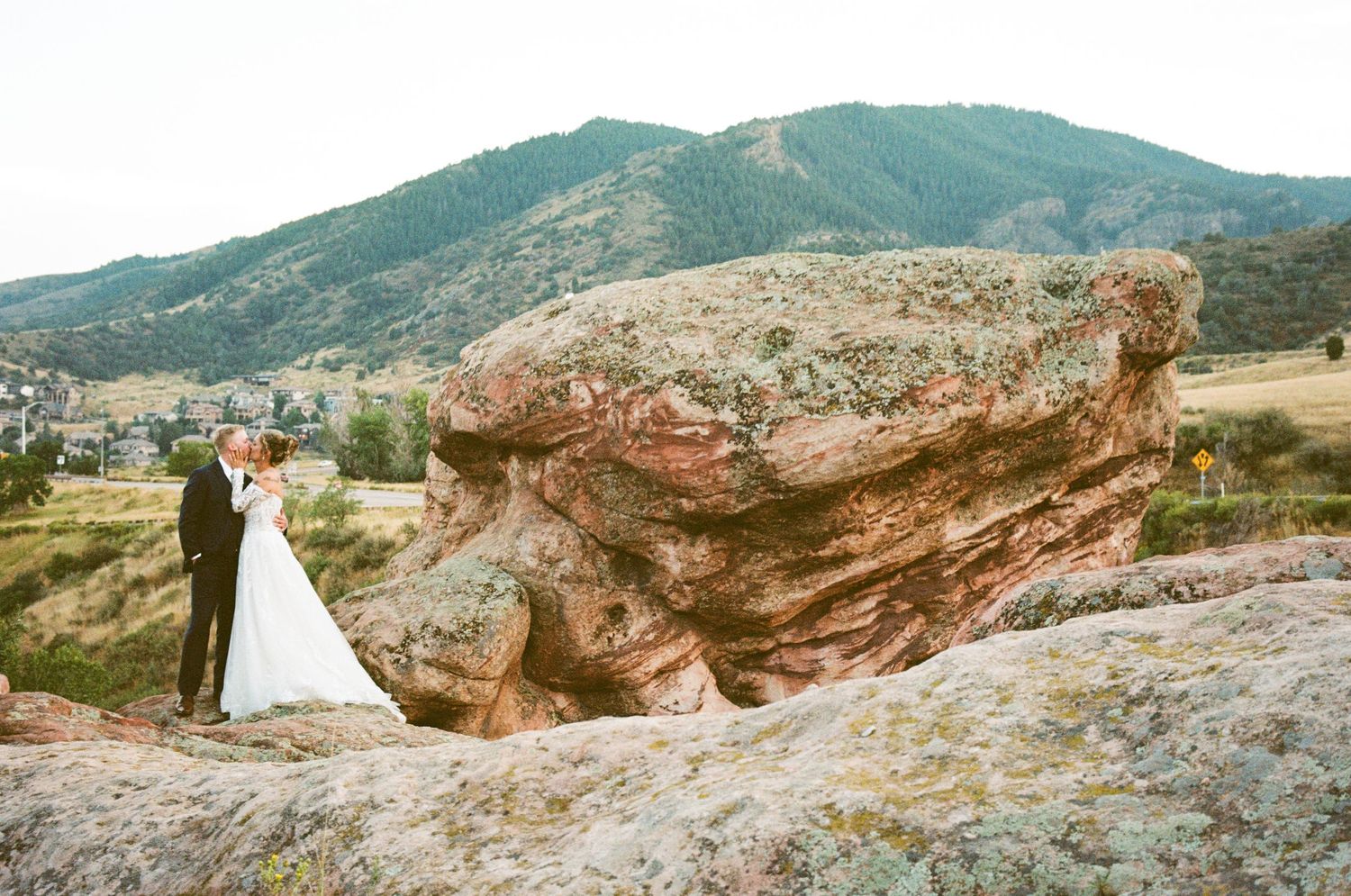 Wedding couple poses against dramatic red rock formation in mountain landscape.