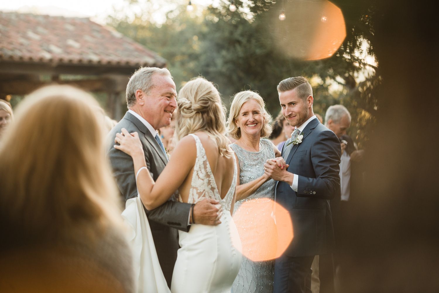 Romantic outdoor wedding reception with couples dancing during golden sunset.
