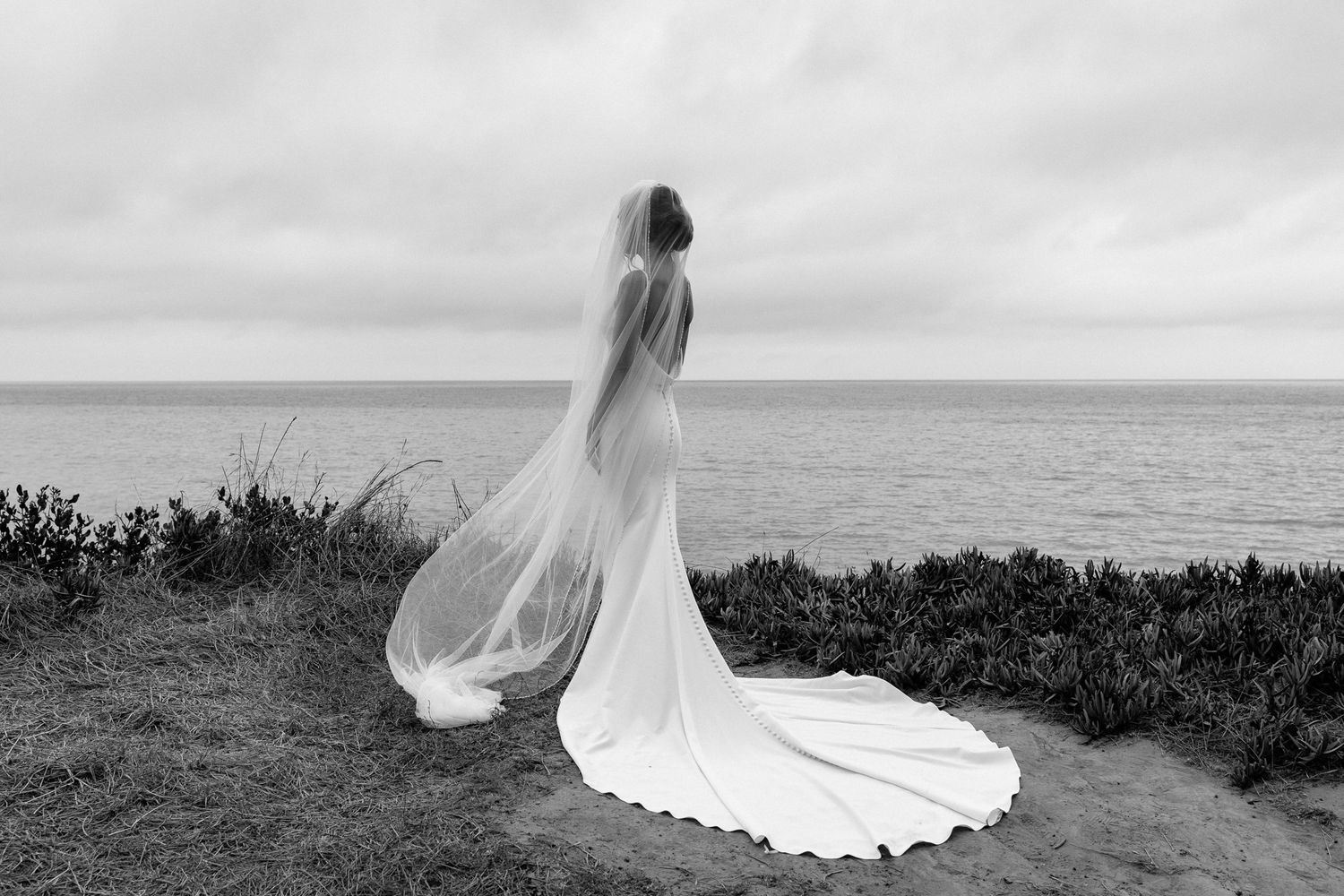 Dramatic silhouette of wedding dress and veil against ocean backdrop.