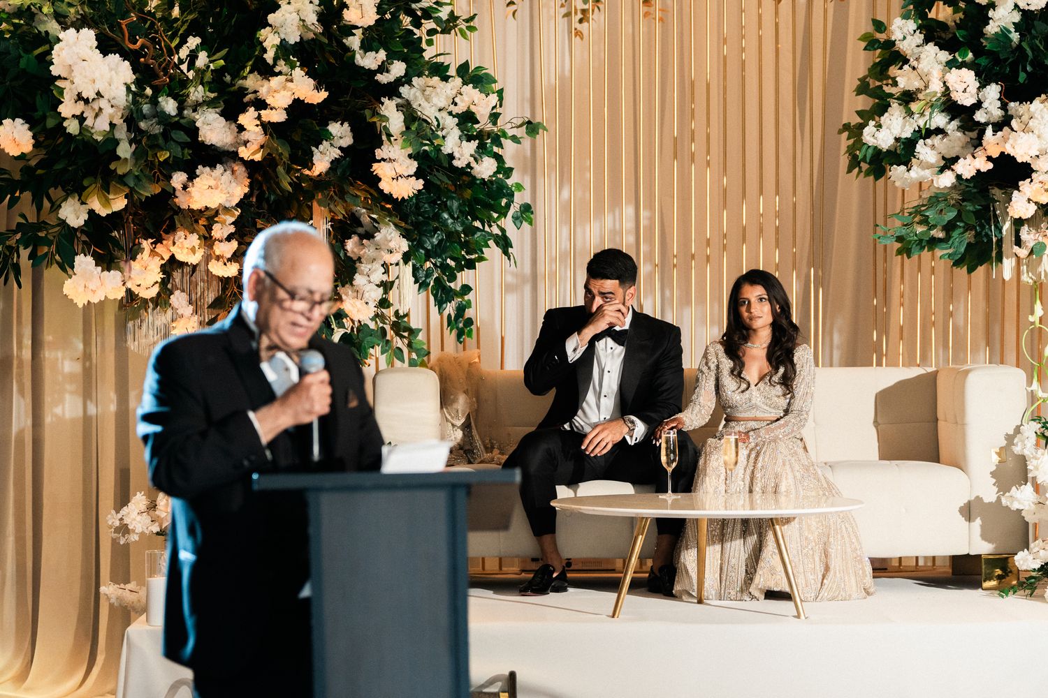 Elegant wedding reception venue decorated with white floral arrangements and warm lighting.