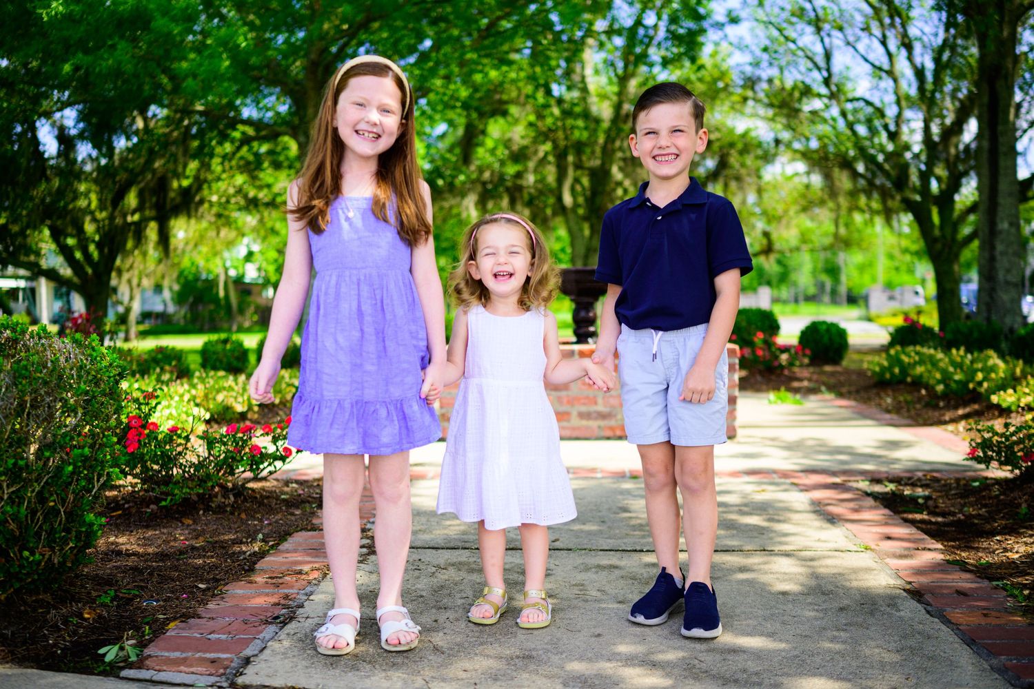 Children in spring outfits standing together on garden pathway surrounded by greenery.