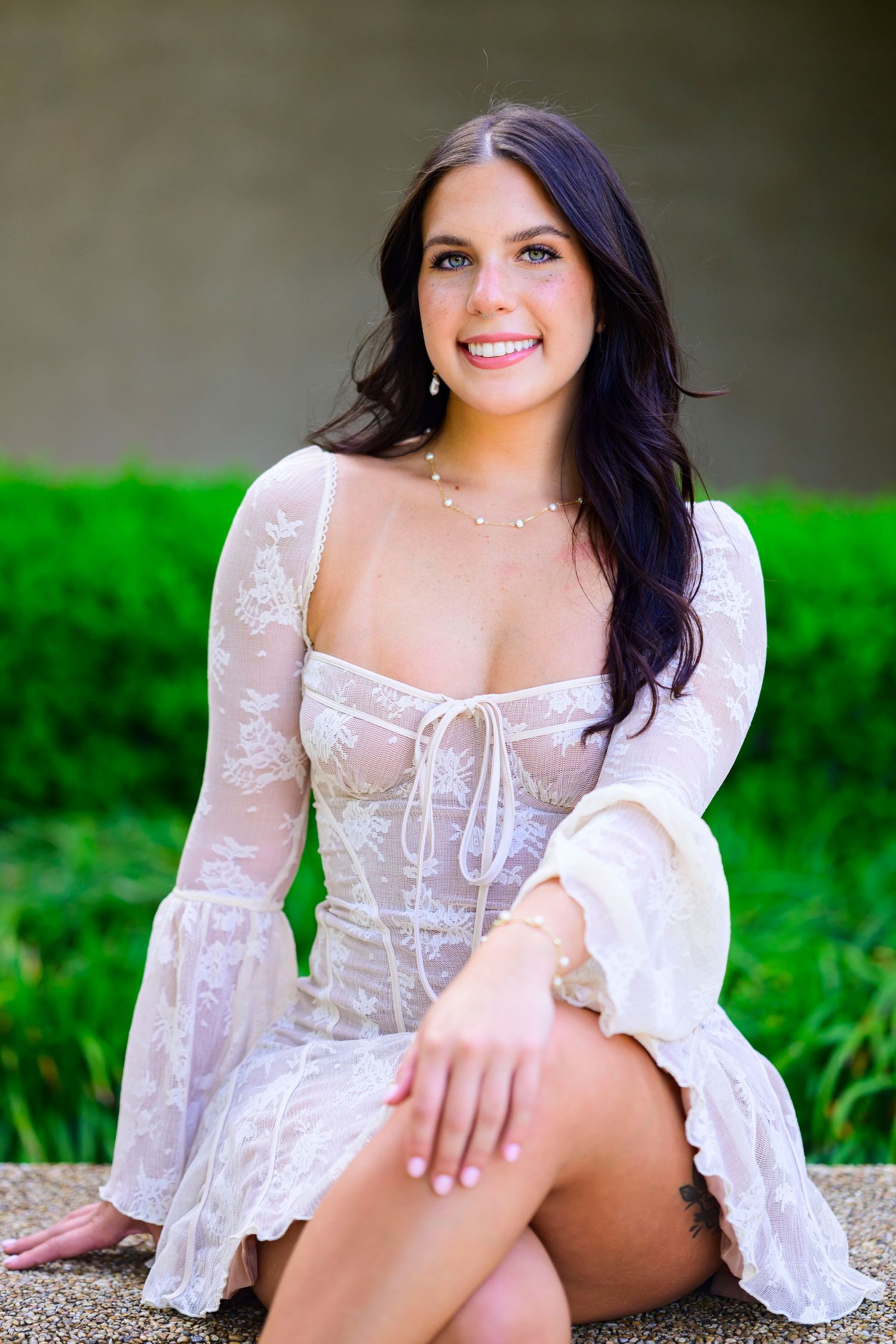Portrait of woman in white lace dress sitting outdoors against natural background.