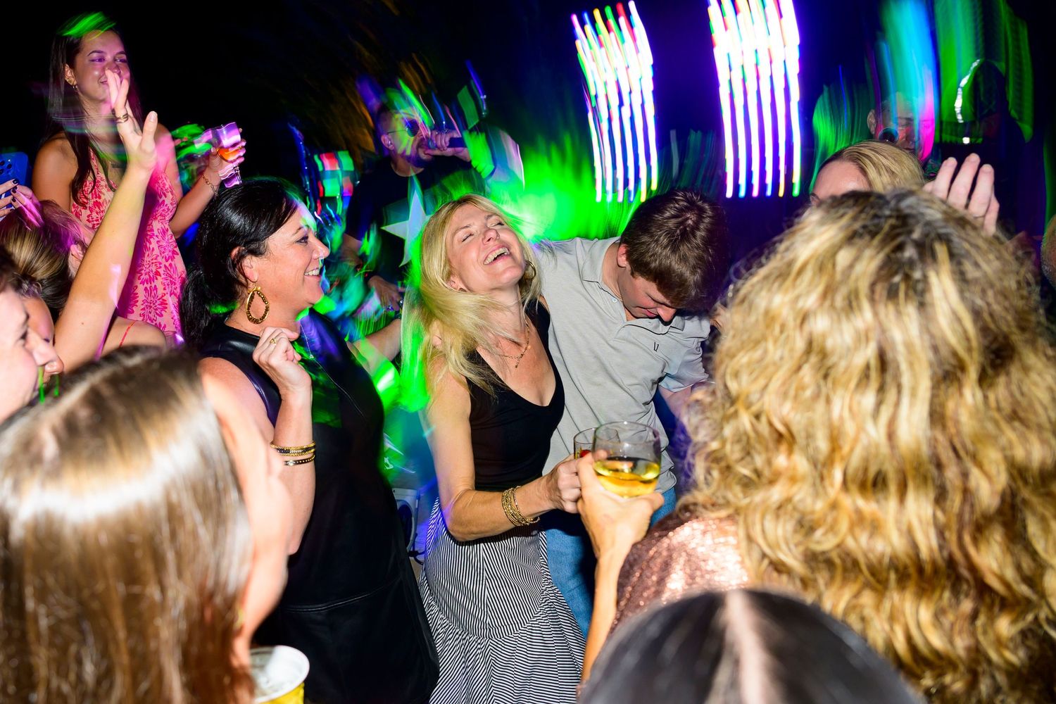 Crowd of partygoers dancing under colorful lights with white fountain sparklers in background at nightclub event.