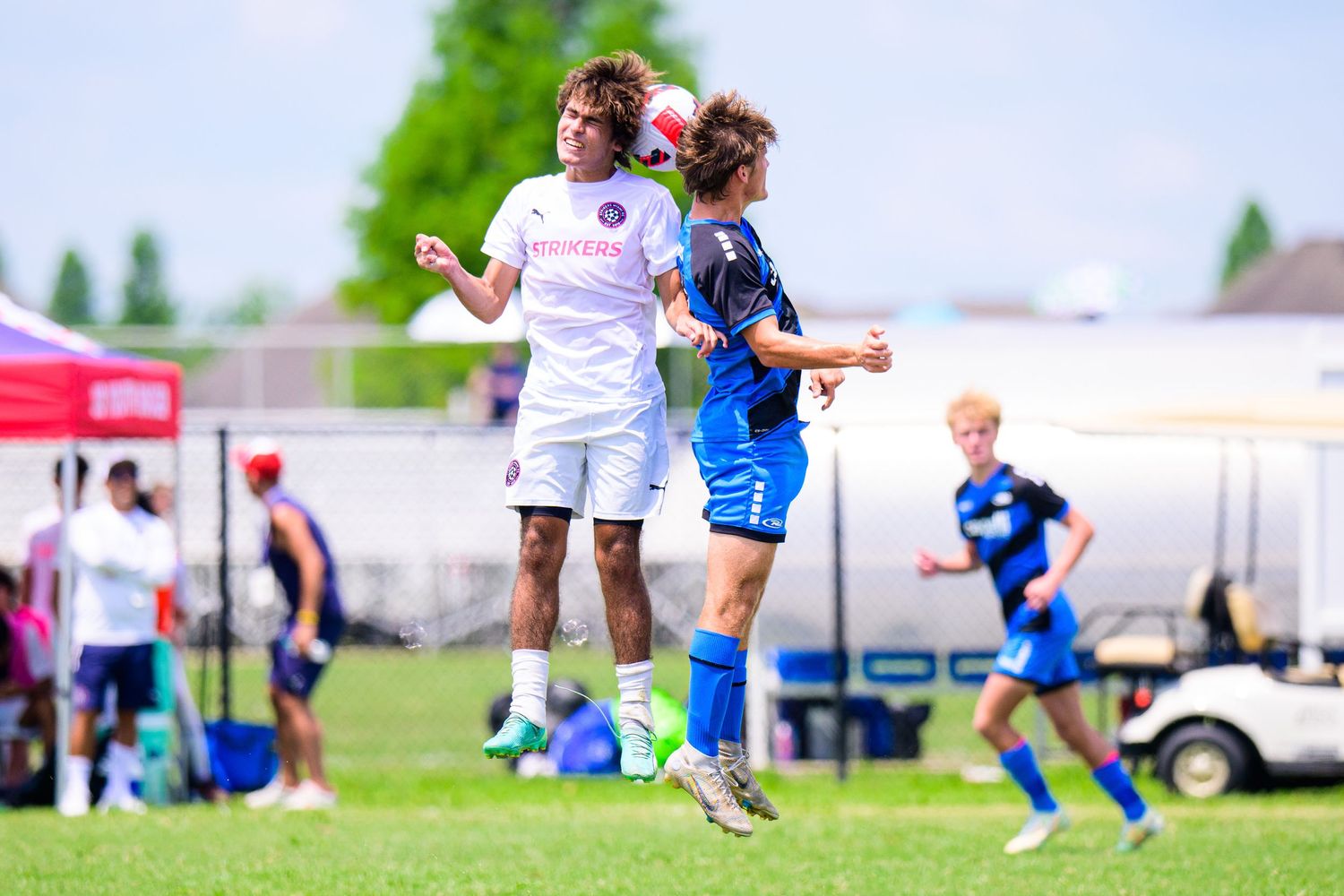 Two soccer players jump high to compete for ball during match with spectators watching.