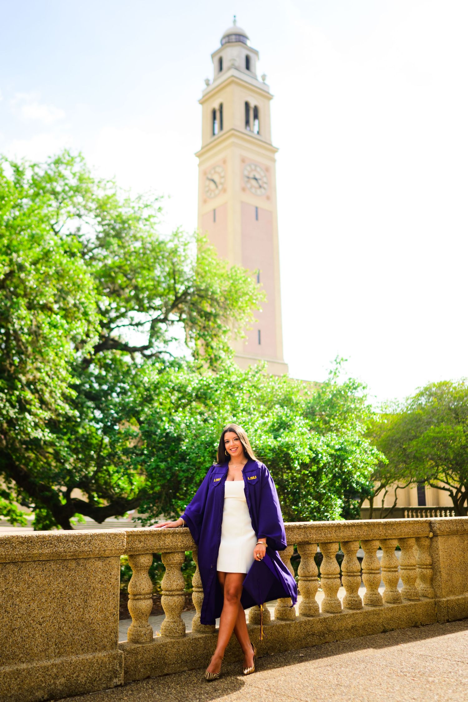 LSU graduate poses in purple robe by Memorial Tower at Louisiana State University campus.