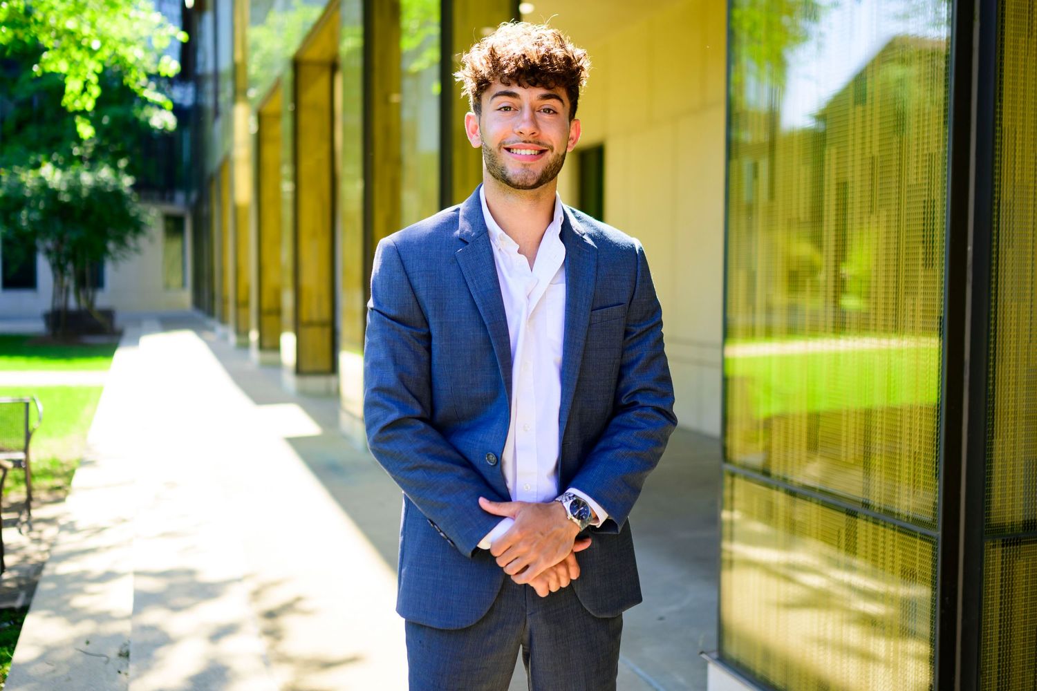 Professional portrait of person in navy suit against modern building exterior.