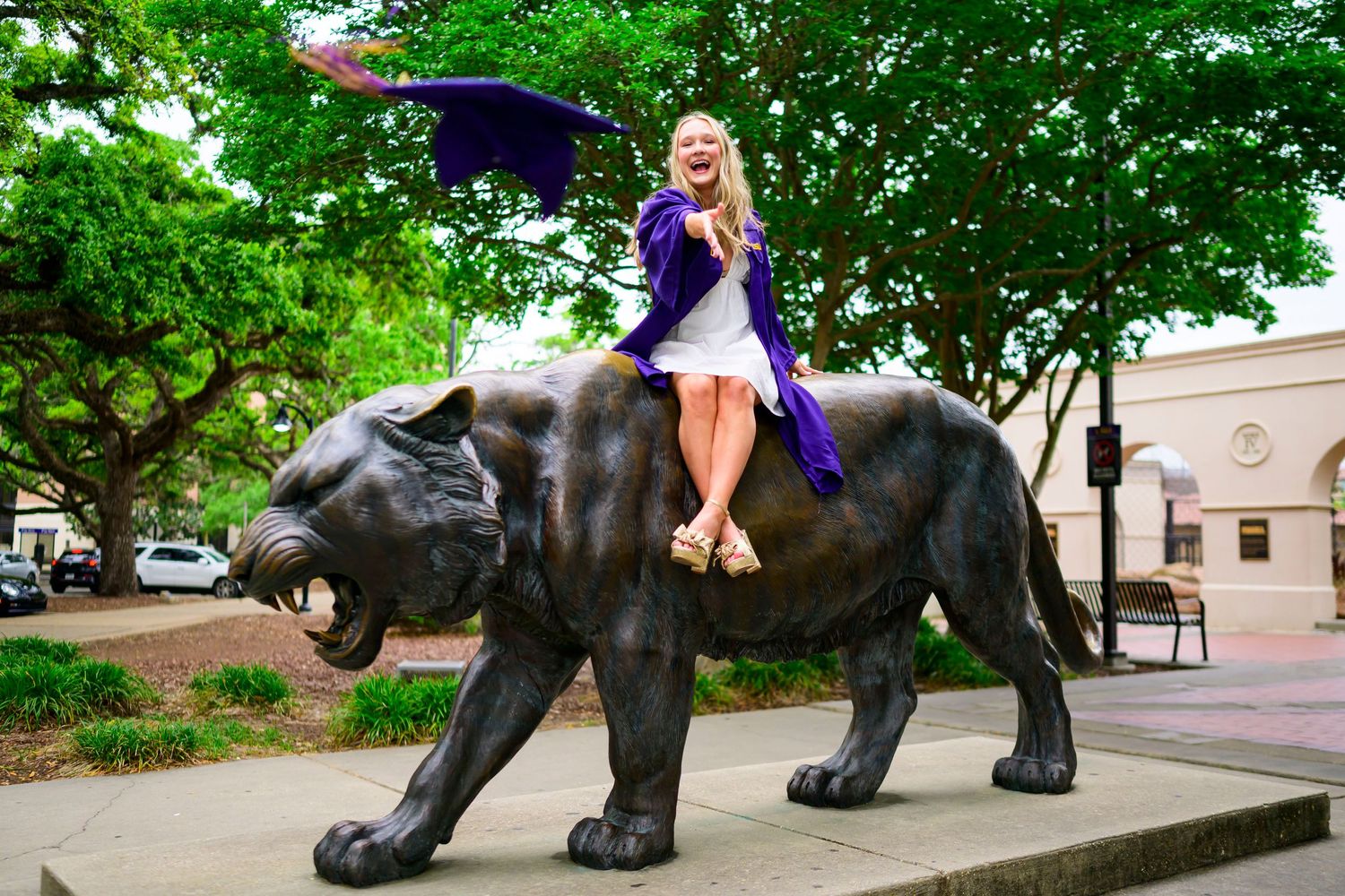 Student sits atop a large bronze panther statue on a university campus.
