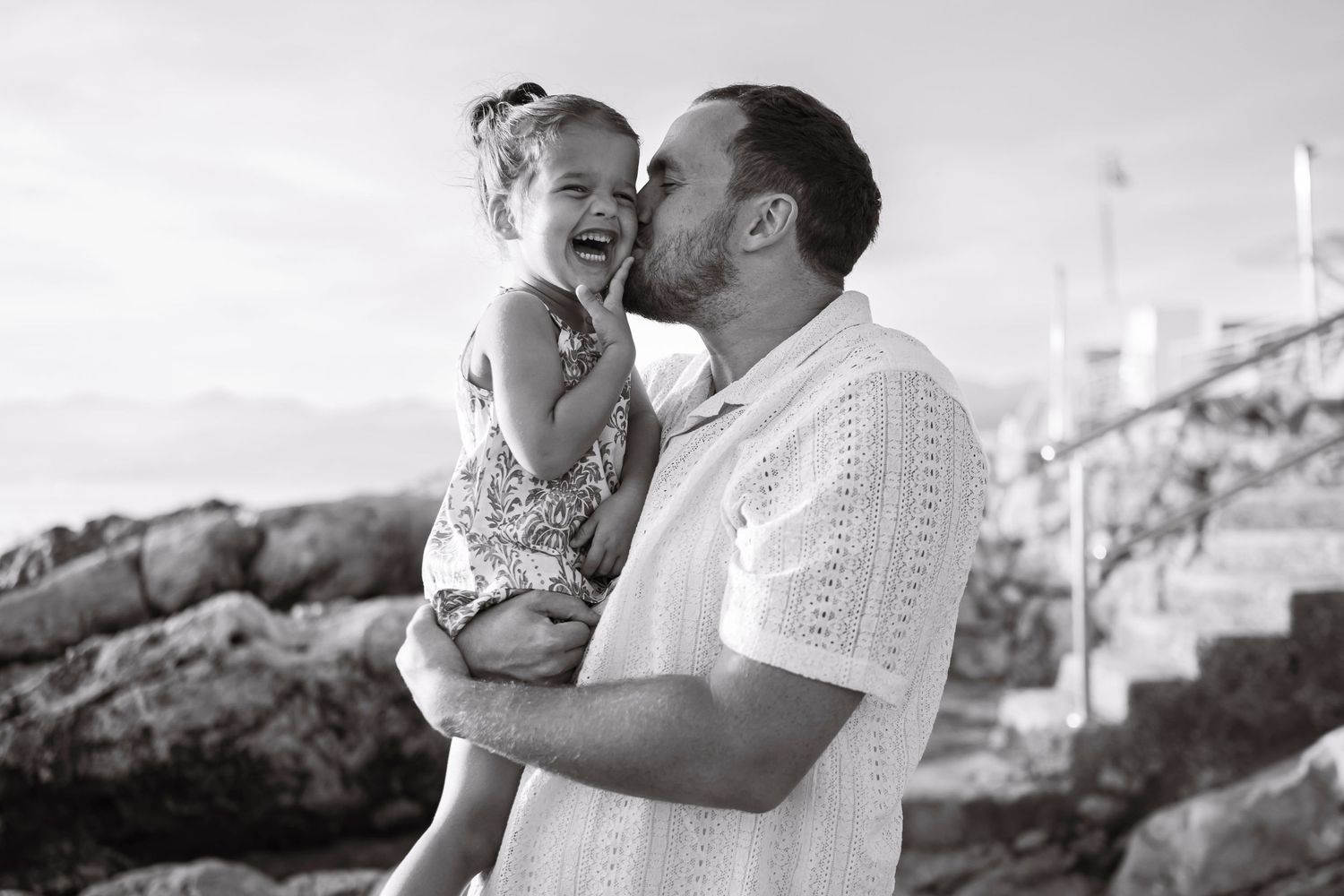 Black and white portrait of joyful moment between parent and child on rocky coastline.