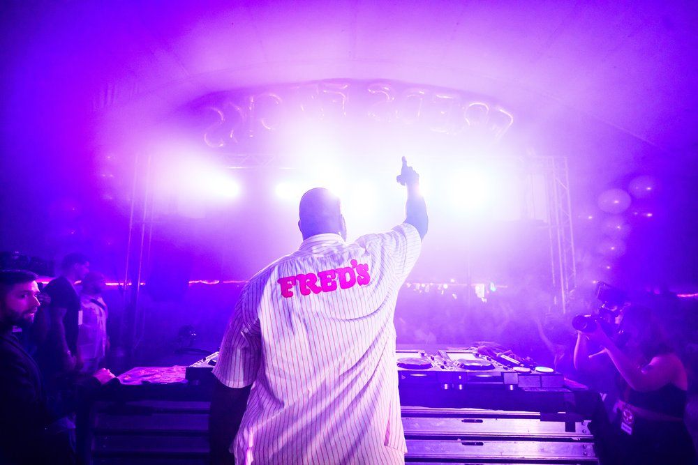 DJ performing at concert with bright purple stage lighting and smoke effects.