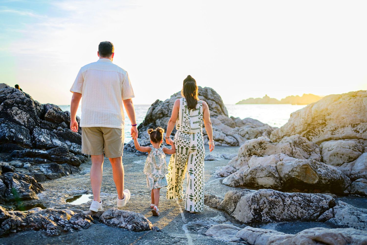 Family exploring rocky coastal area at sunset with ocean views in background.