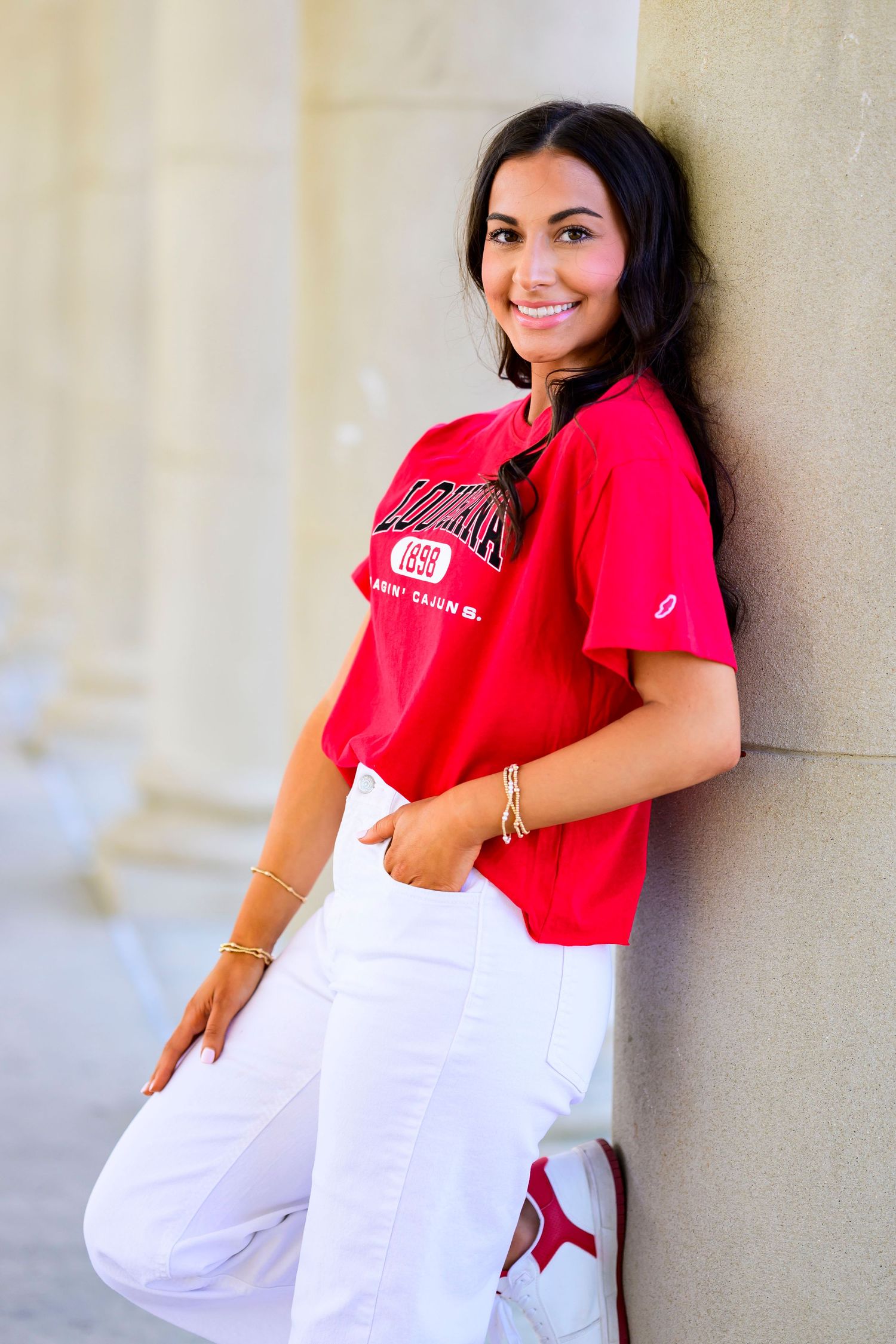 Student in red LSU shirt and white pants poses against light colored wall.