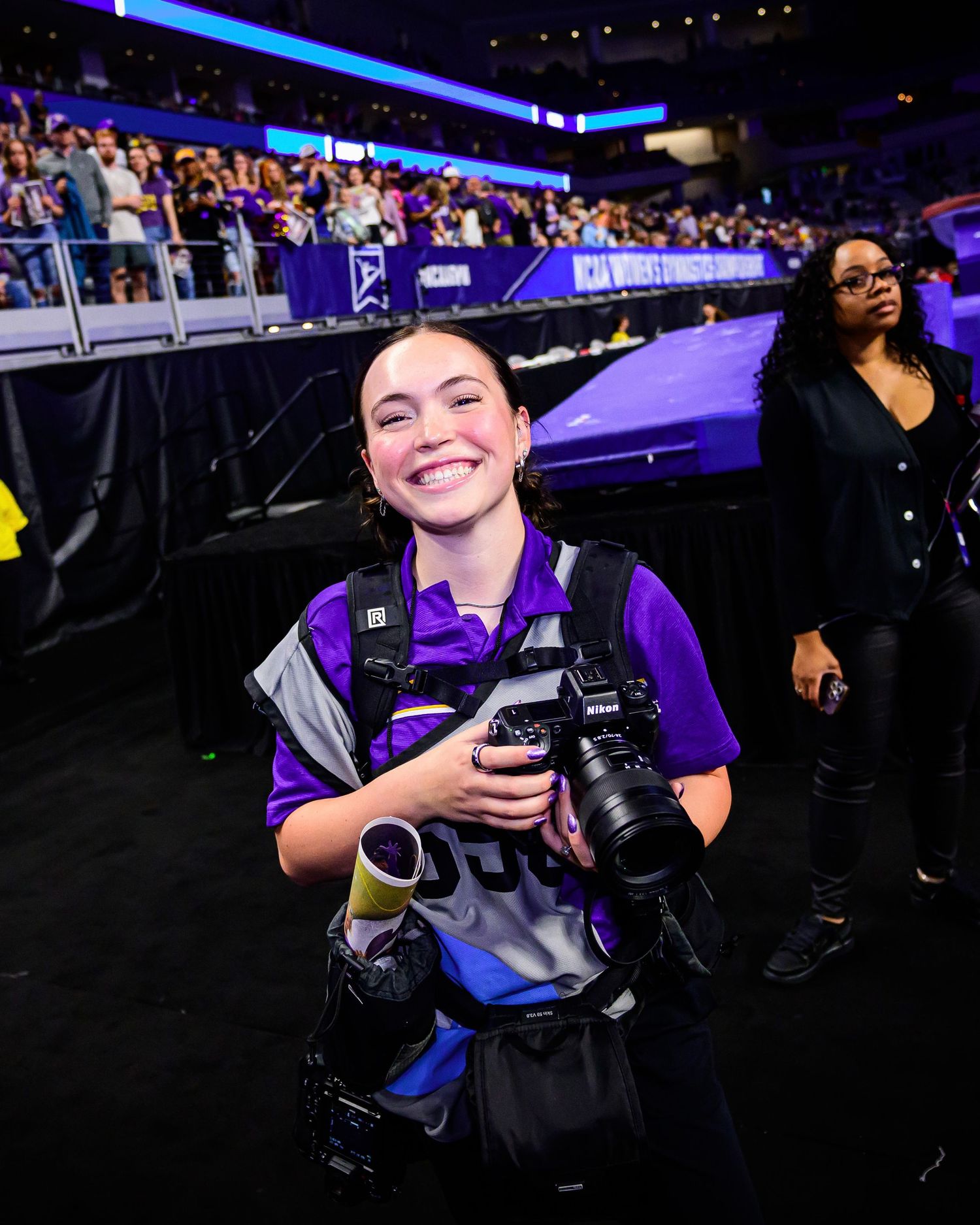 Professional photographer with camera at sports event capturing game action in arena with purple lighting.