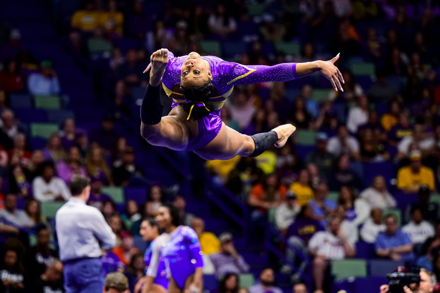 Gymnast performs mid-air split leap in purple leotard during LSU competition.