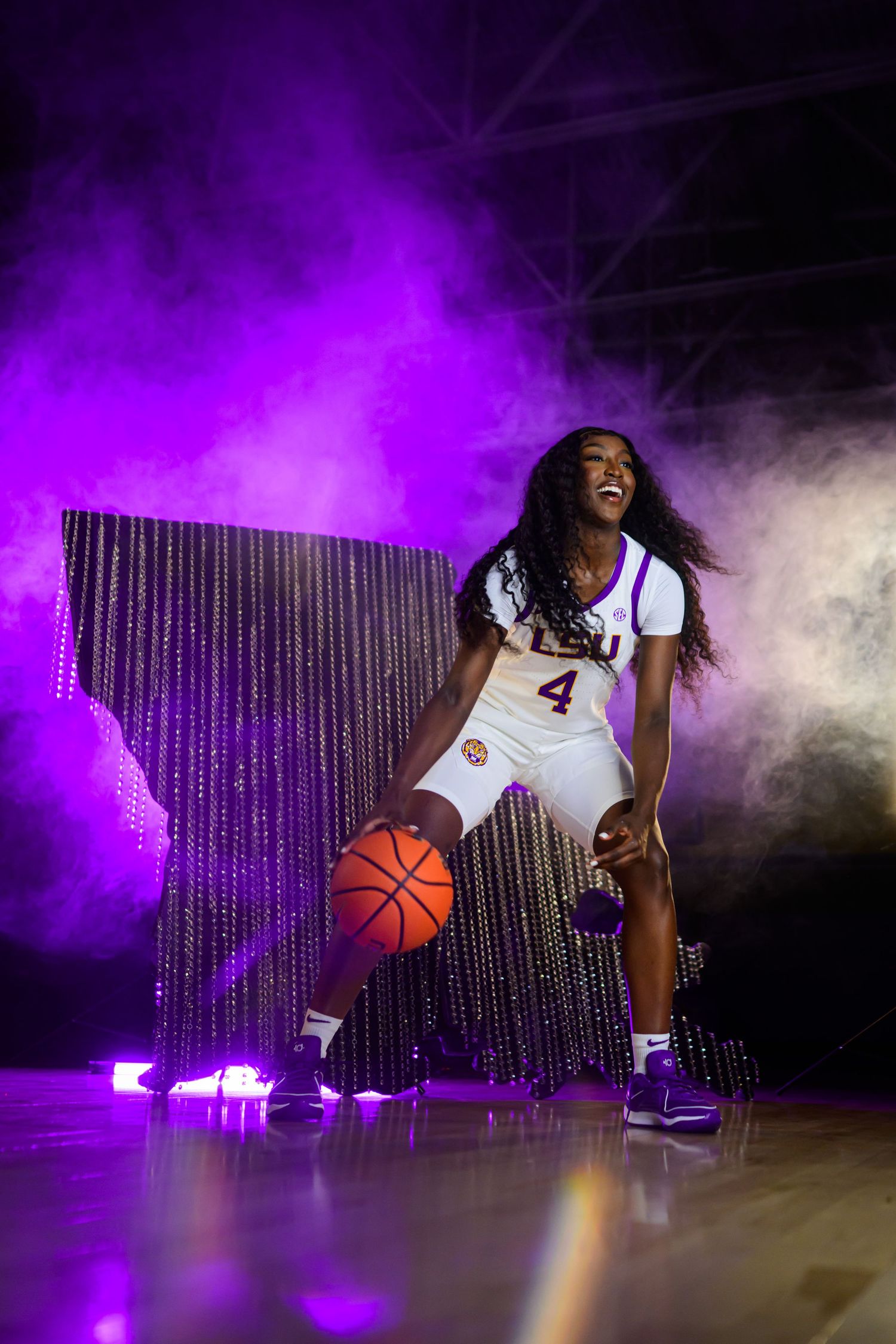 Basketball player poses with ball against purple lighting and sparkly backdrop.