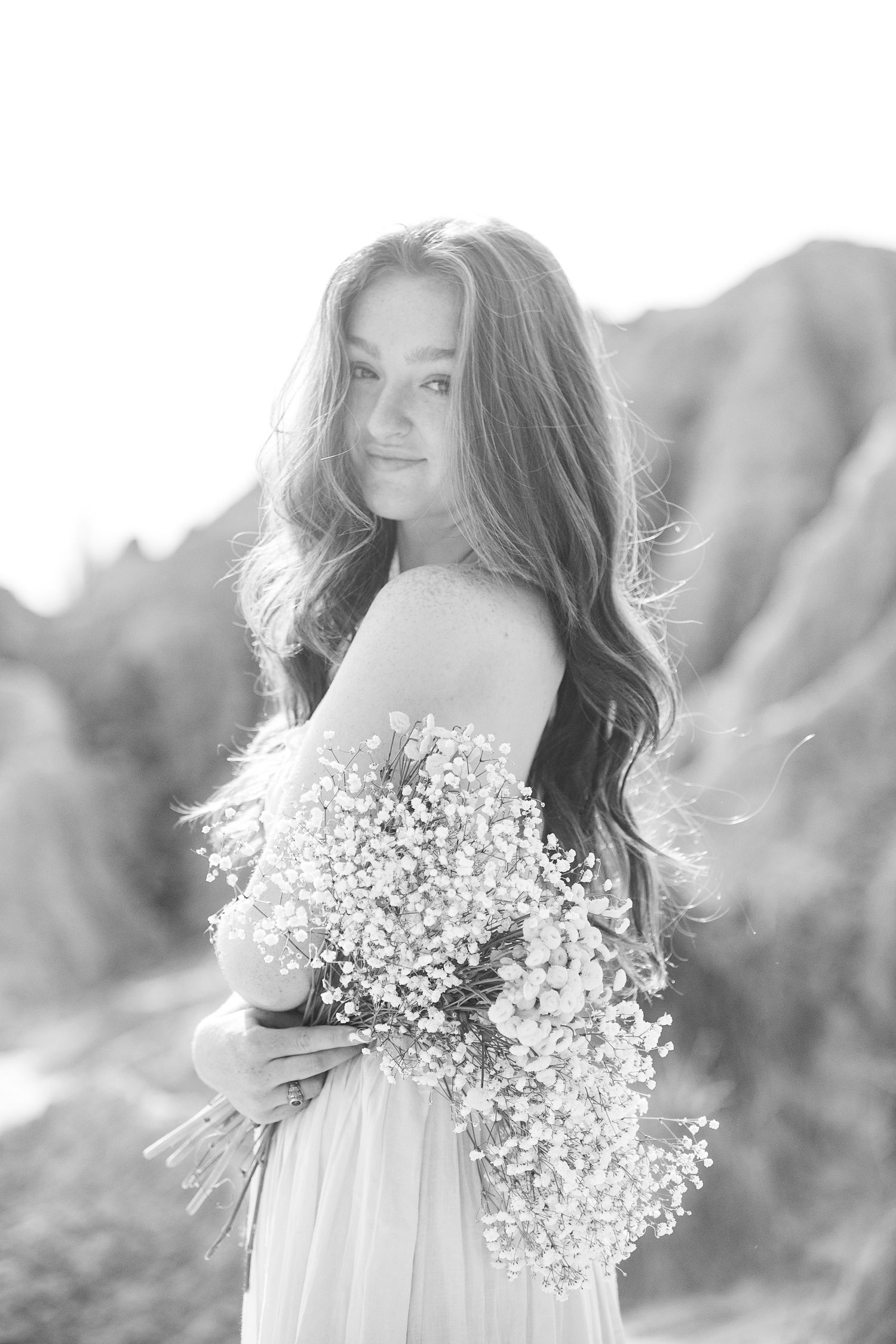 A dreamy black and white portrait of a young woman holding baby's breath flowers in a flowy dress.