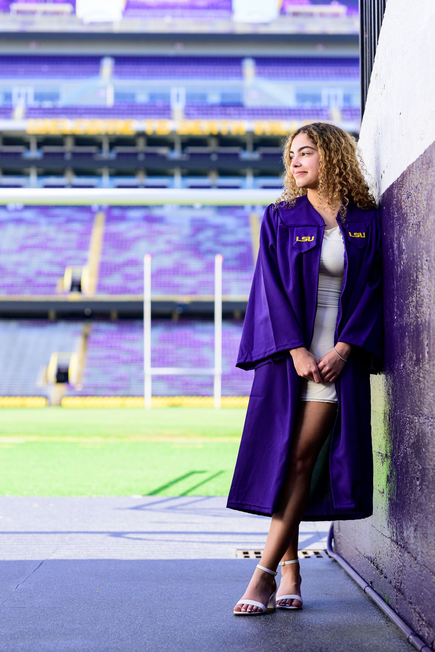 Graduate posing in a purple LSU graduation gown against stadium backdrop.