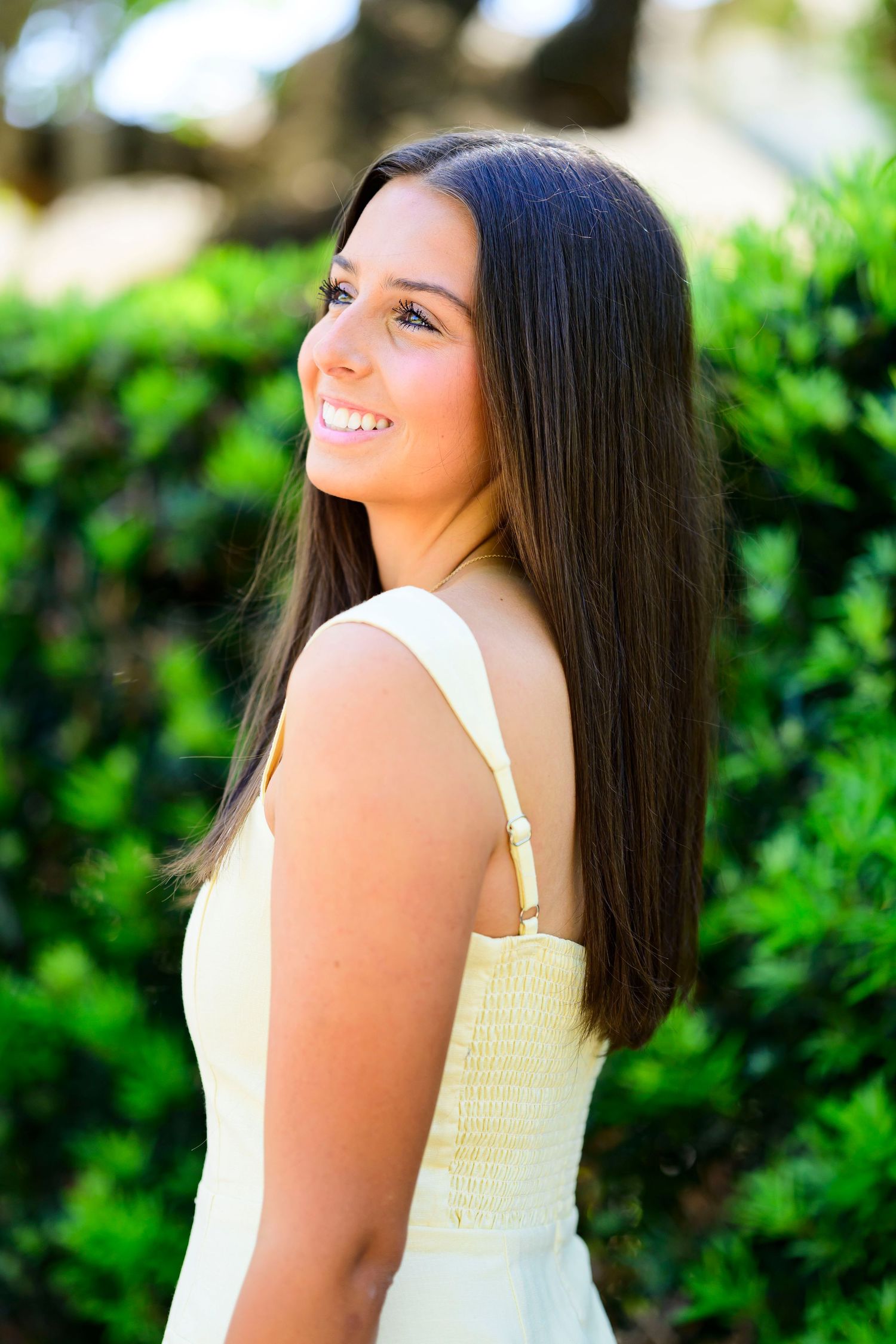Portrait of graduate in white dress against lush green garden background.