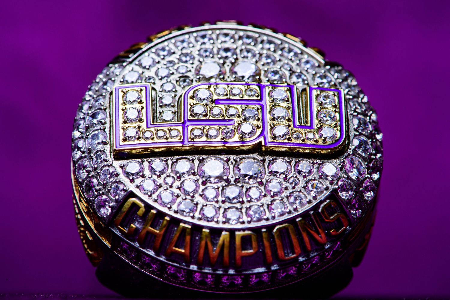 Close-up of diamond-encrusted LSU championship ring against purple background.