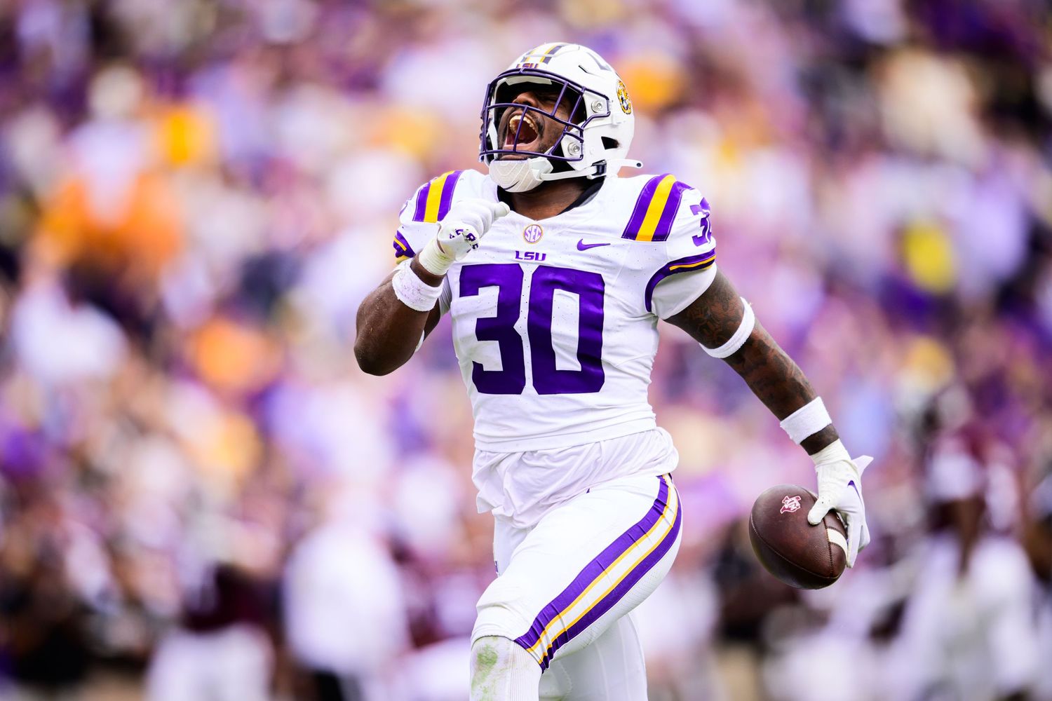 LSU football player in white uniform running with ball during game.